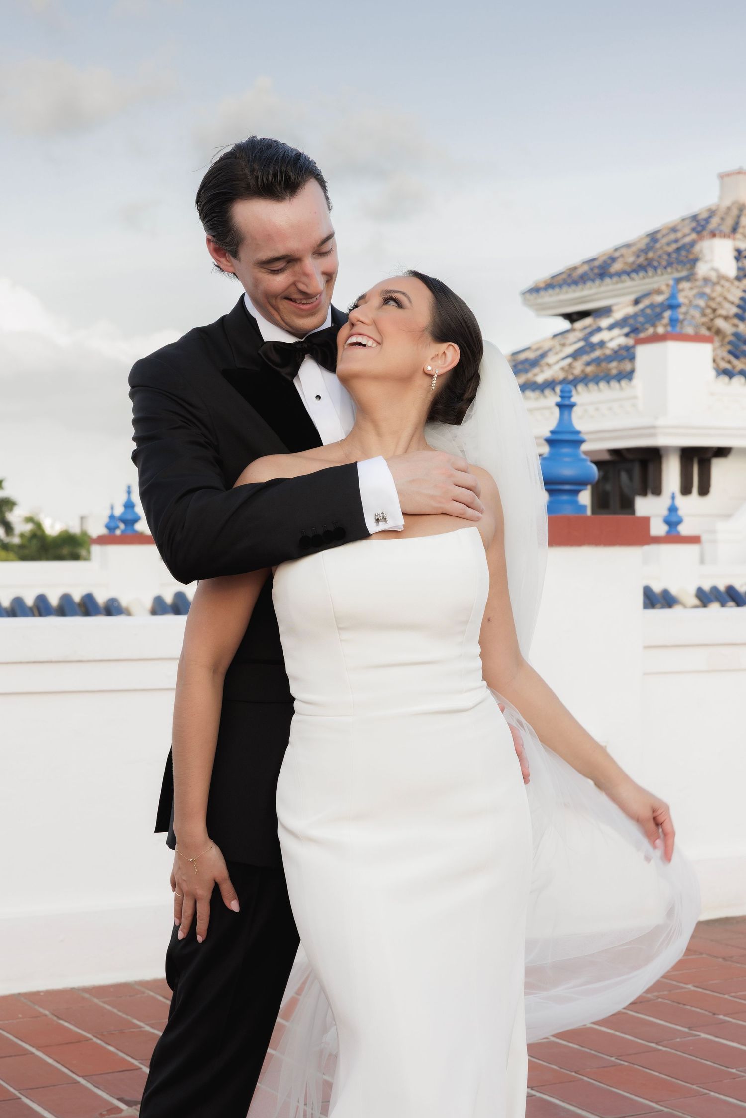 Romantic wedding couple dancing on a terrace with Spanish colonial architecture in the background.