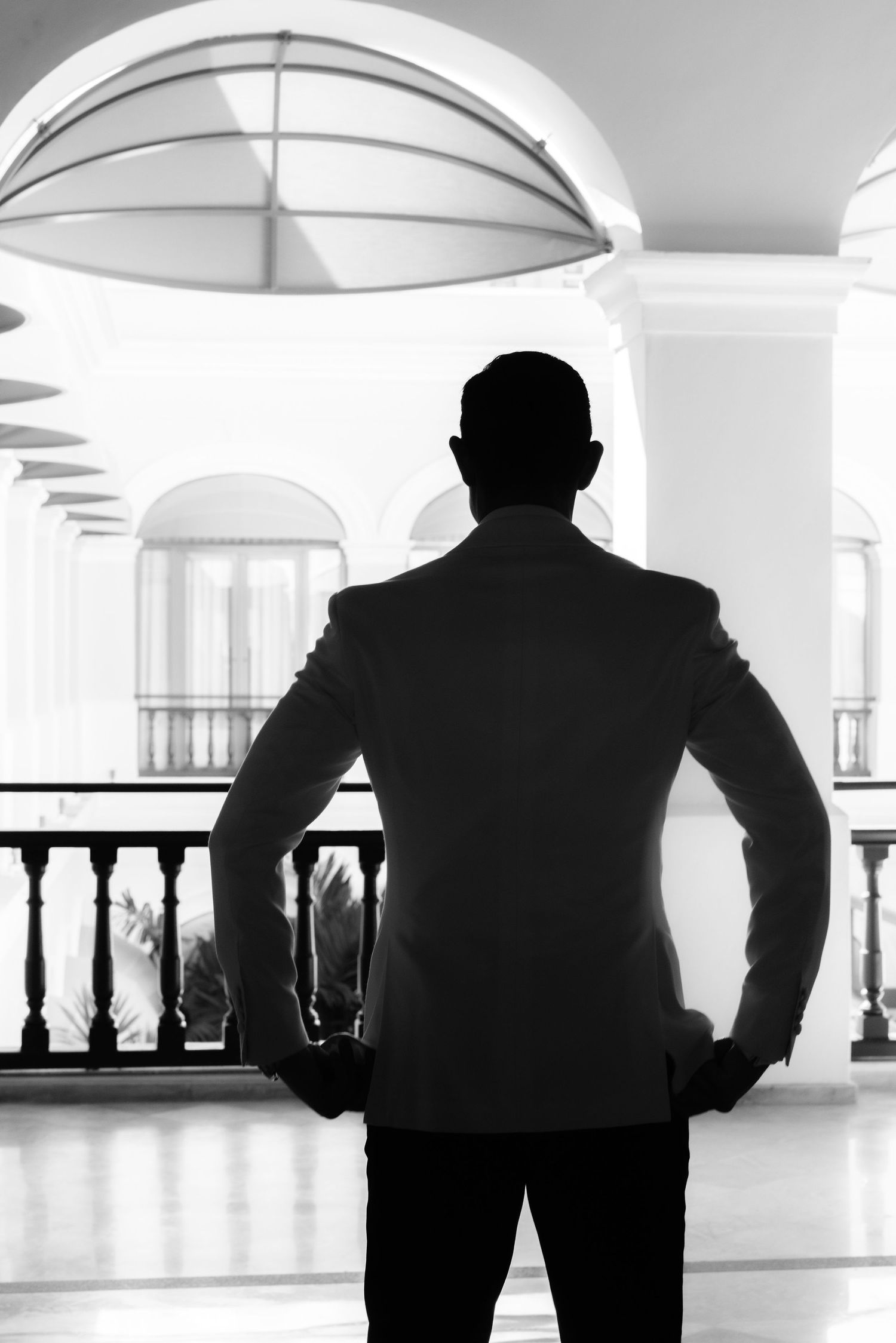 Silhouetted figures stand against white arched windows in a historic building interior.