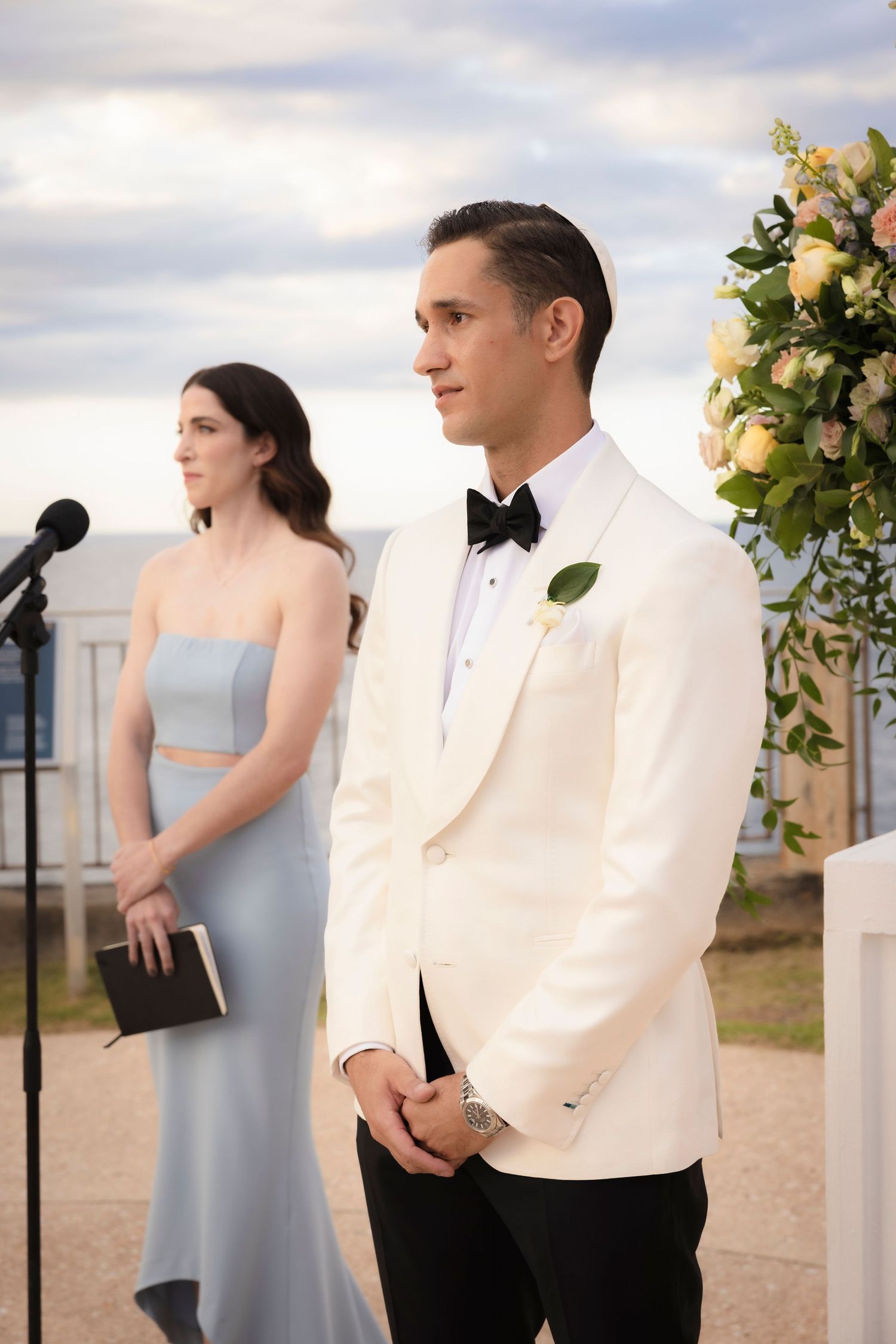 Wedding ceremony setup with white floral arrangements against cloudy sky.