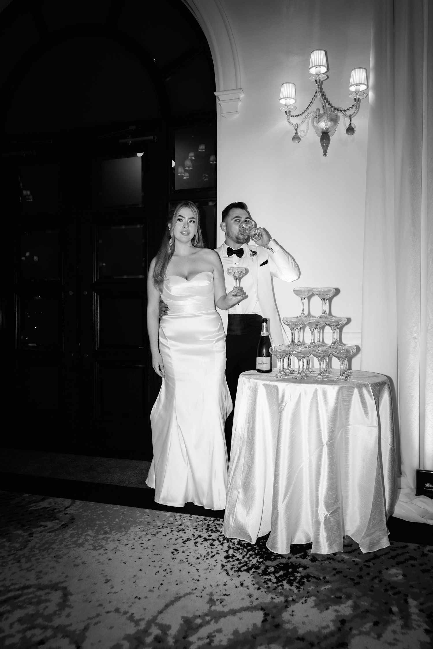 Black and white photo of a champagne tower being filled at an elegant reception.