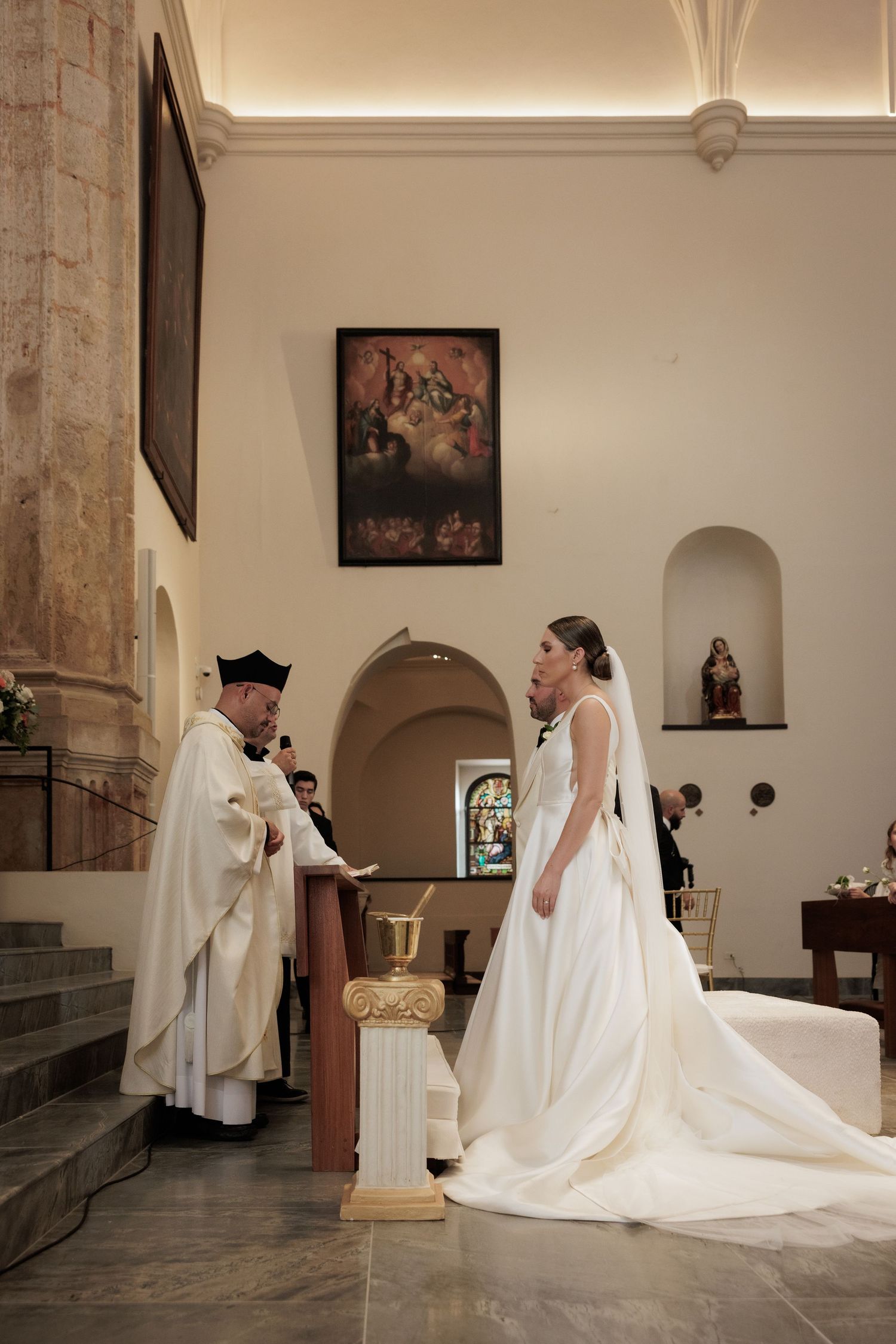 Wedding ceremony in an ornate church interior with white gown and religious officiant.