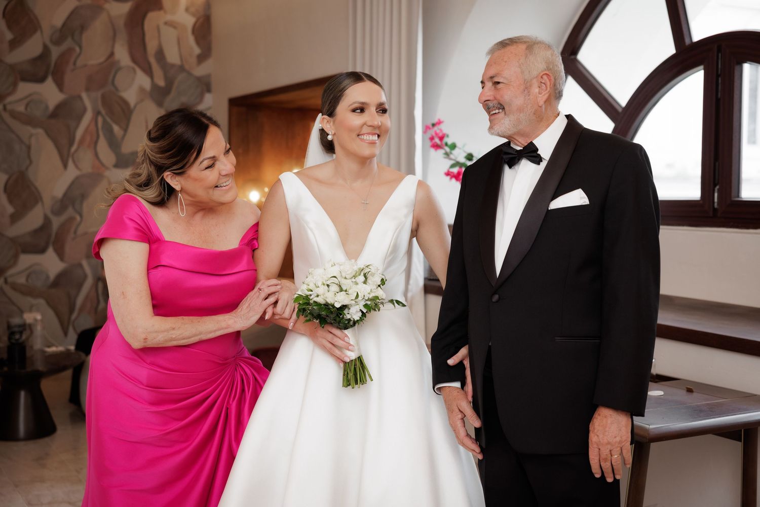 A wedding party poses together in formal attire with the bridesmaids wearing bright pink dresses and white bouquets.