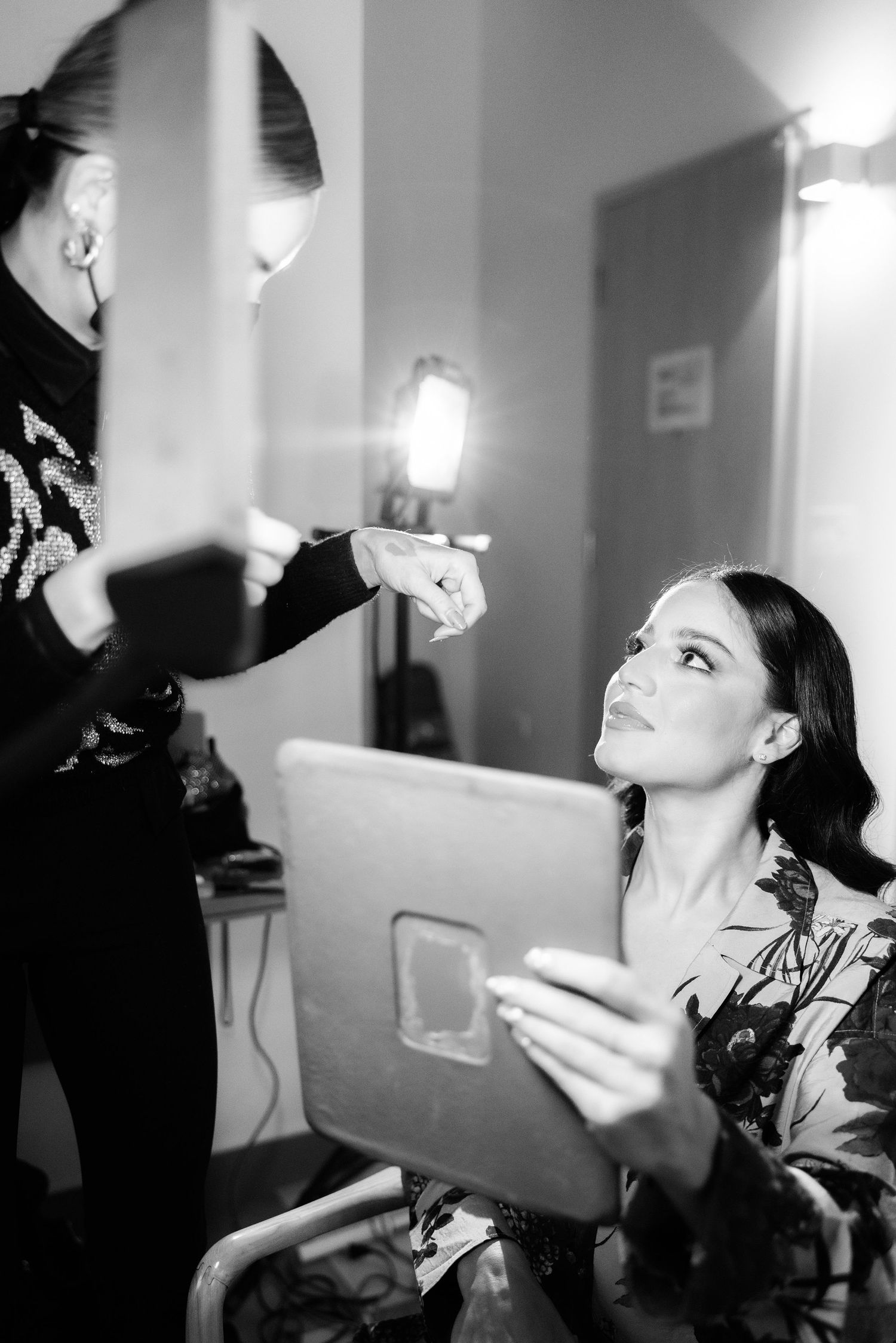 Black and white photos show bride getting makeup done while sitting in chair during wedding preparations.