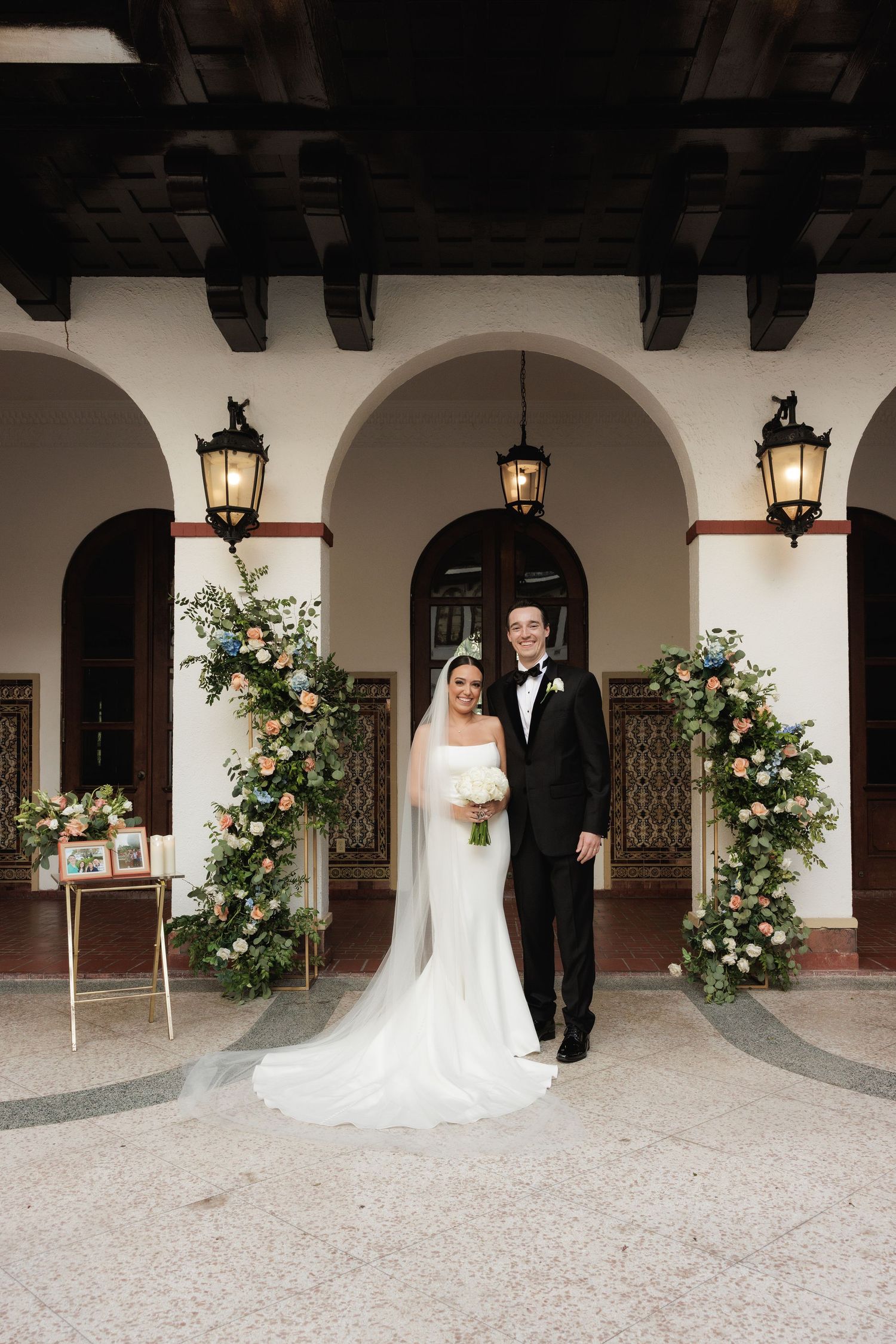 A wedding photo series captured in black and white under elegant archways decorated with floral arrangements.