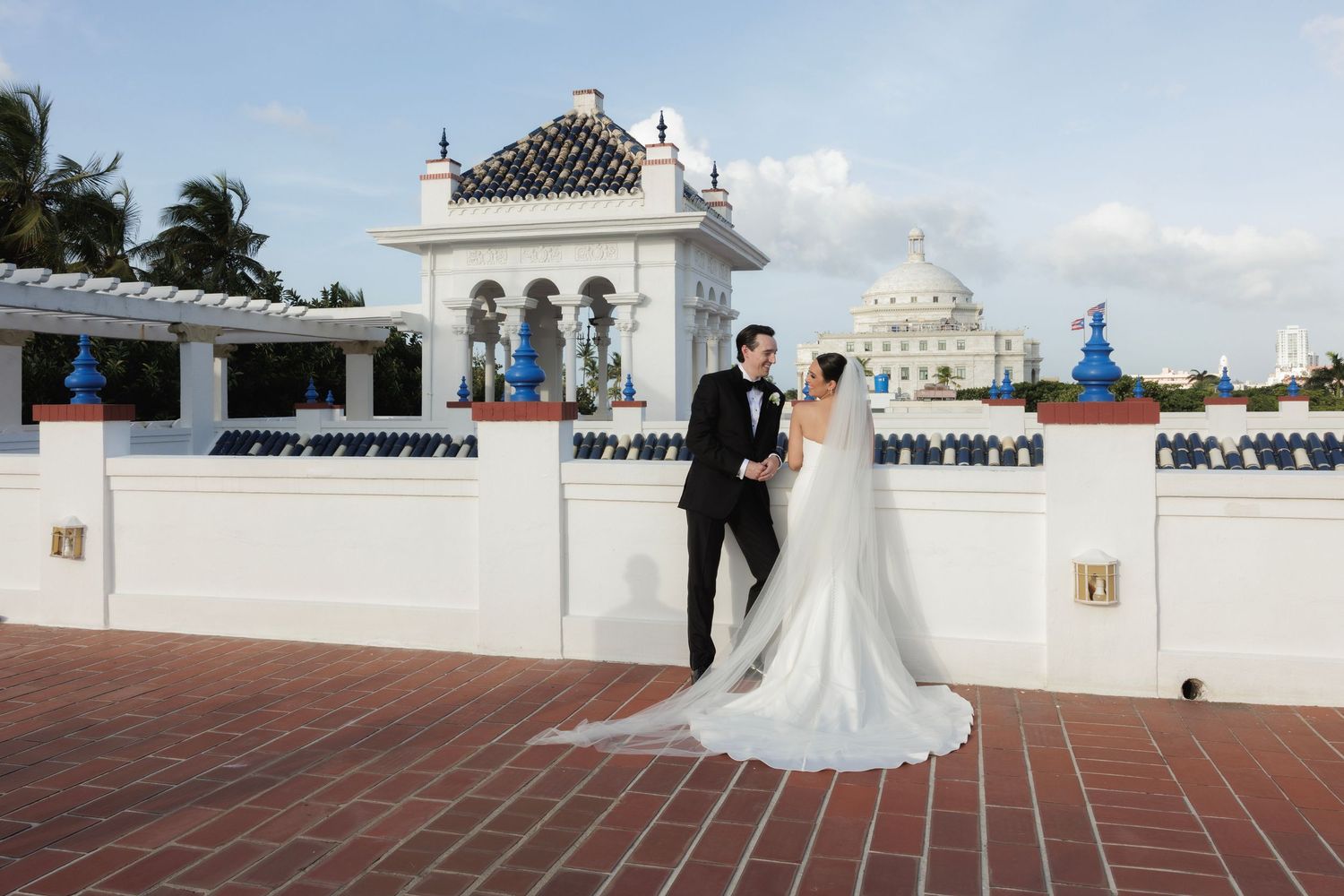 A white wedding dress flowing in the wind against a bright church or cathedral backdrop with white colonial architecture.