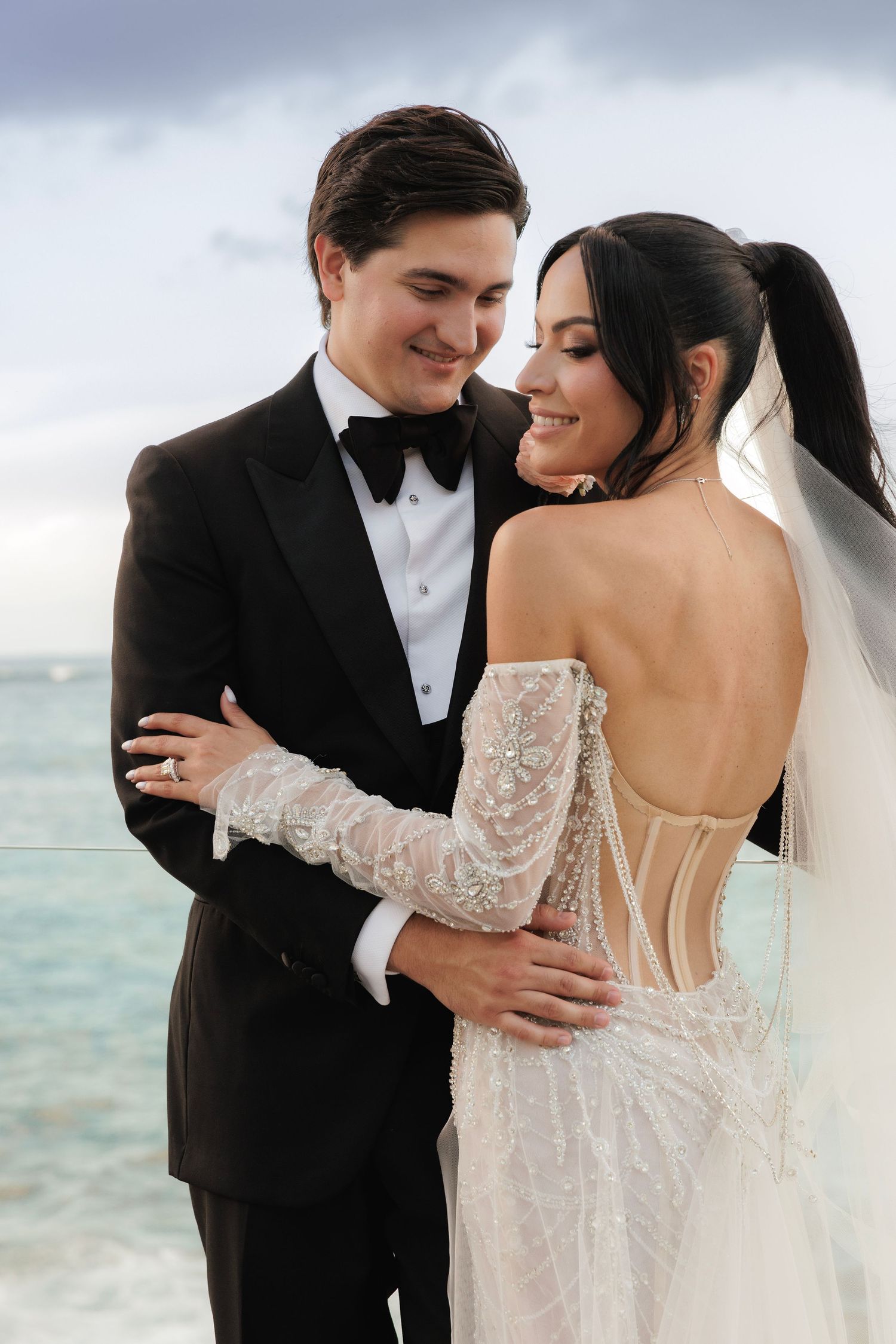 A romantic beachside wedding portrait shows a couple in formal attire against an ocean backdrop.