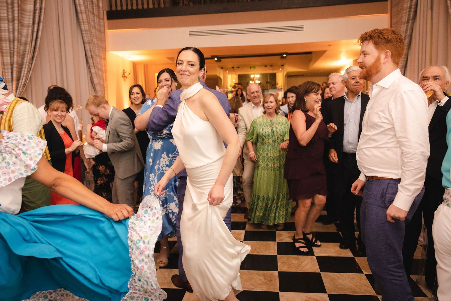 Wedding guests dance together on a black and white checkered dance floor at an indoor reception venue.