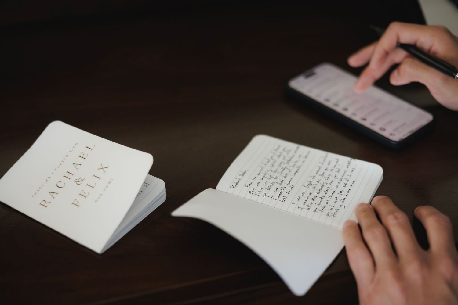 Several hands write in notebooks and papers on a dark wooden table, showing focused study or note-taking activities.