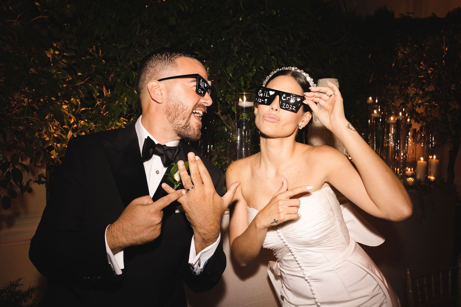 Wedding guests clink glasses for a toast during an outdoor evening reception beneath twinkling lights.
