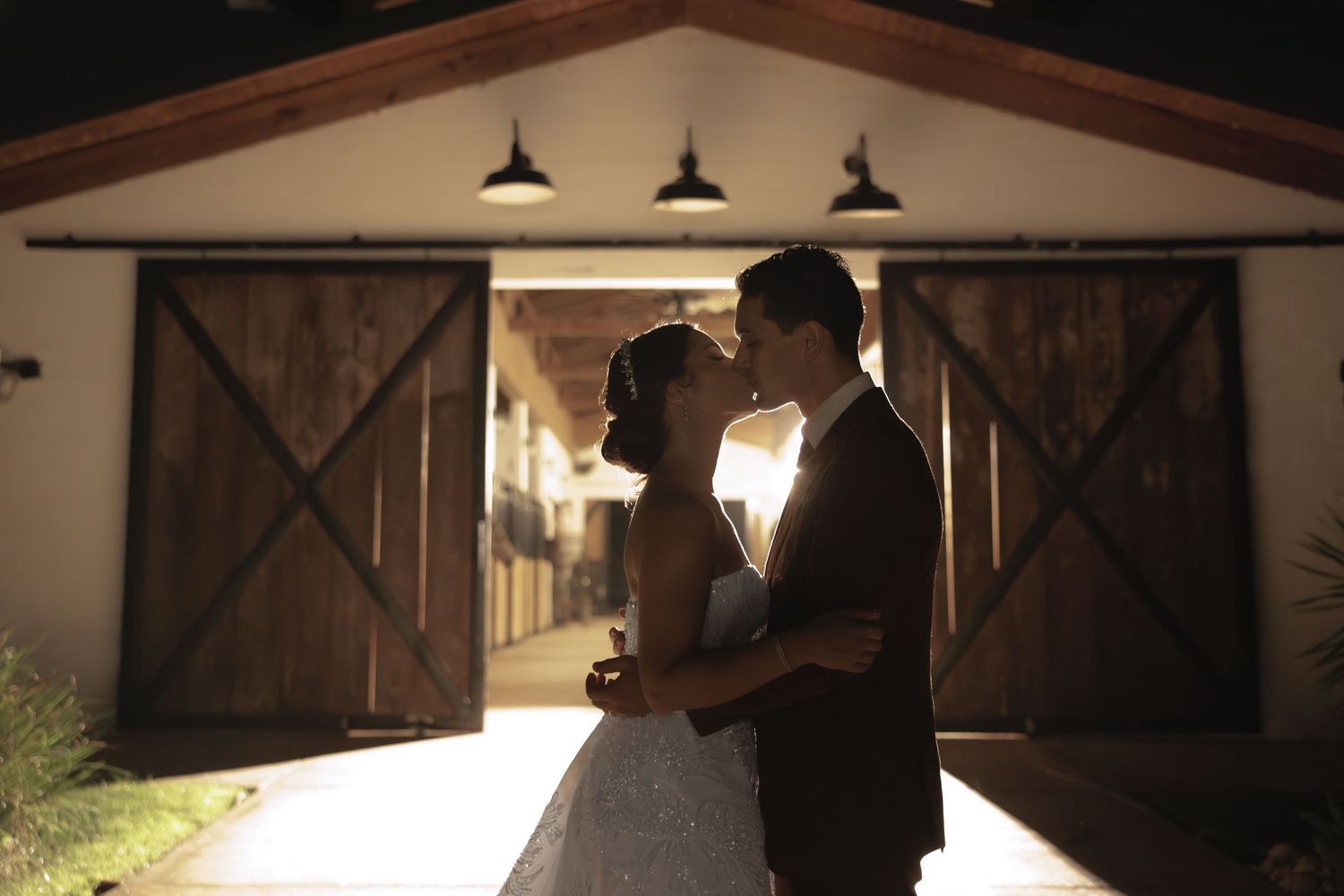 A romantic couple dances together in a rustic barn venue illuminated by warm lighting.