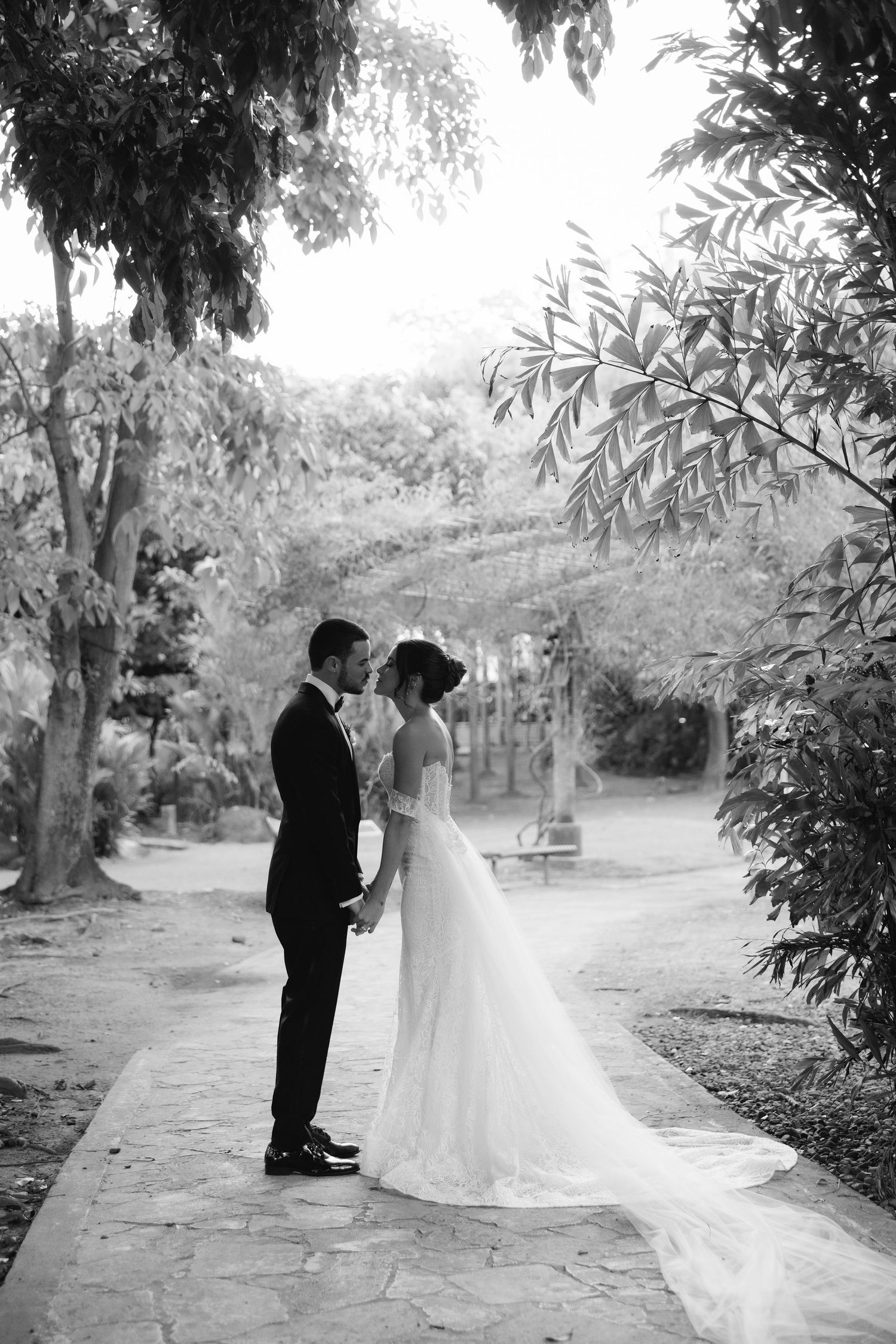 Black and white photo of couple standing on stone path surrounded by lush garden scenery.