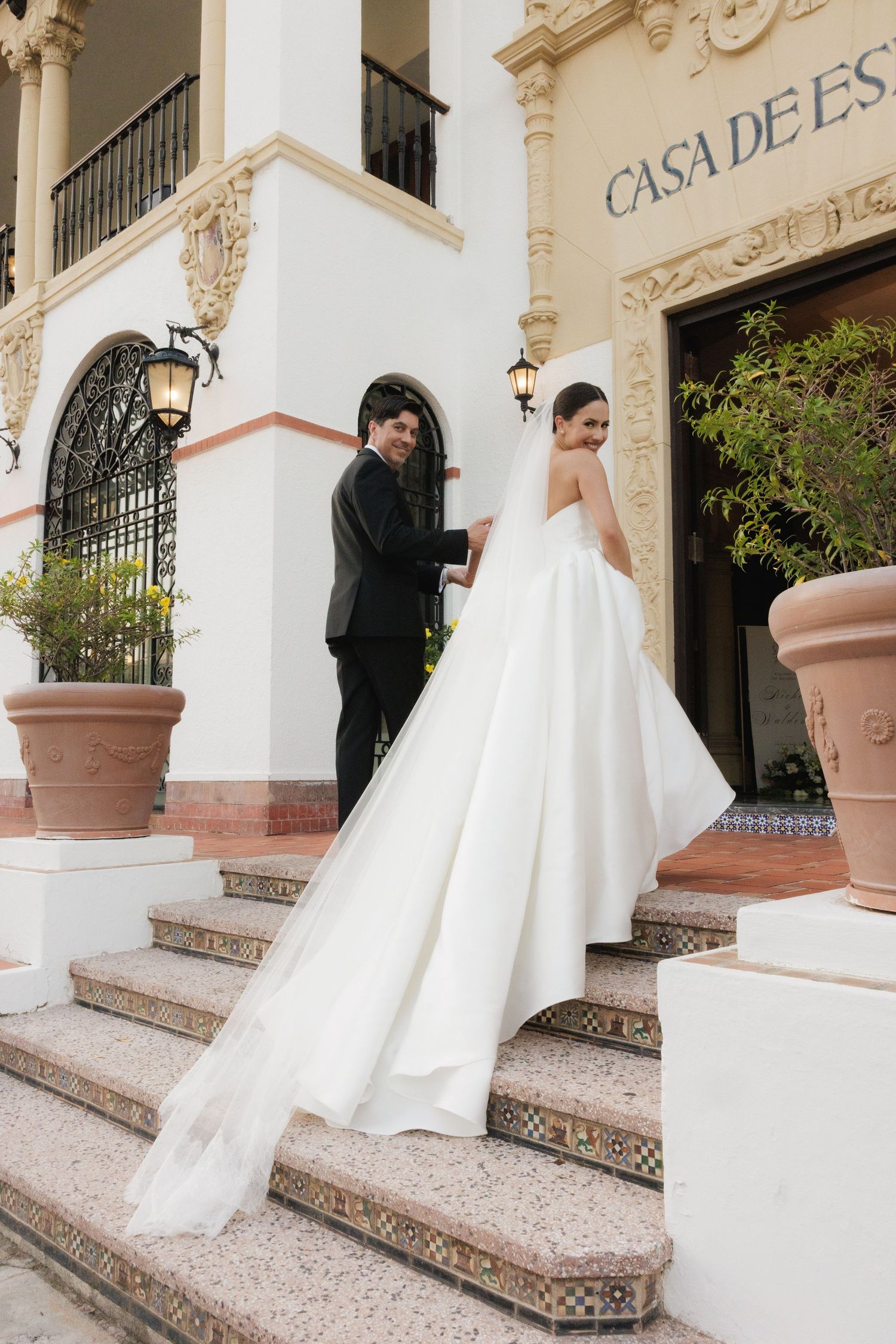 Newlyweds descend ornate stone steps at Casa de España in traditional wedding attire.