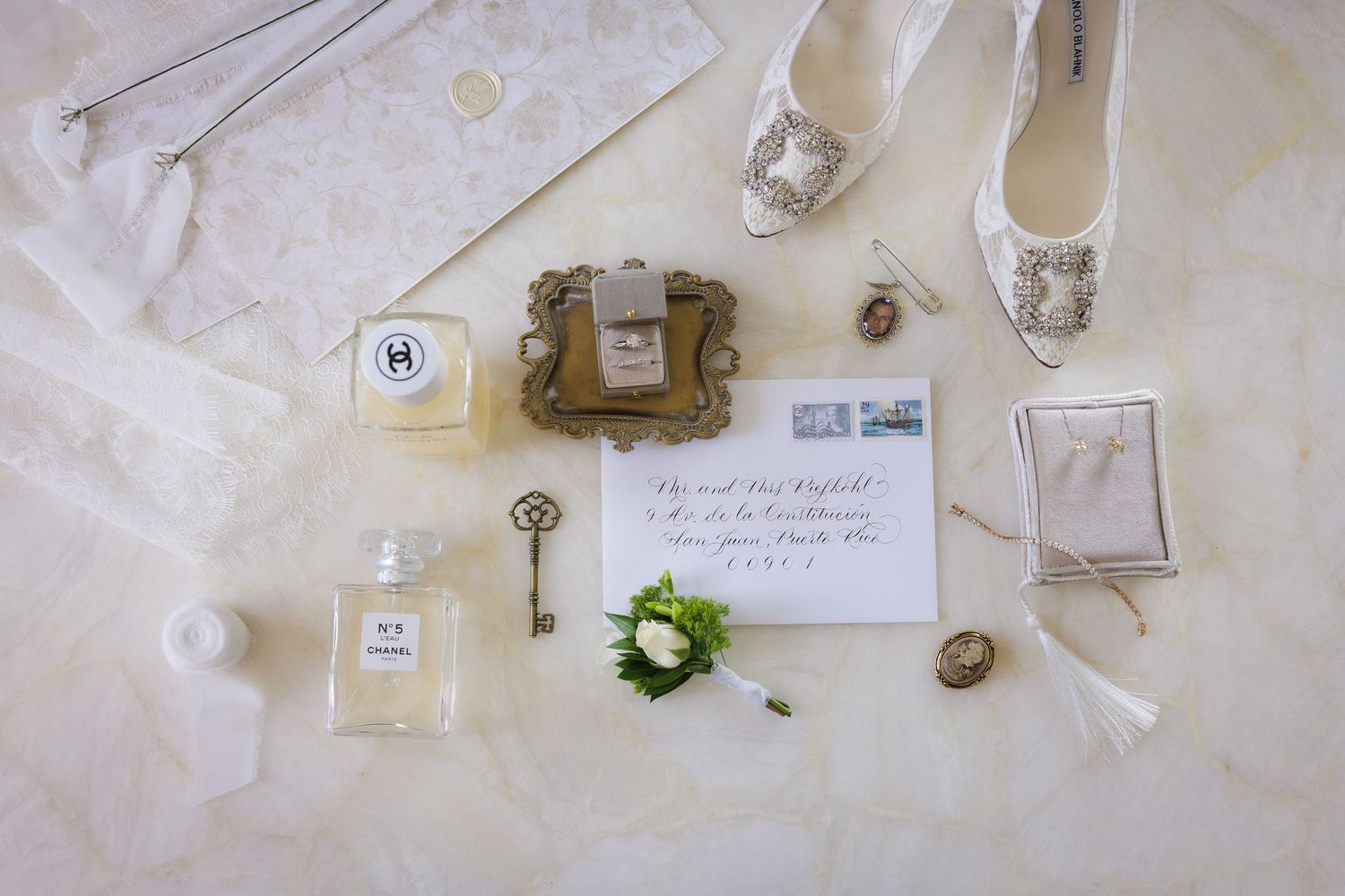 Wedding day details flatlay with perfume, invitation, key, shoes and delicate accessories.