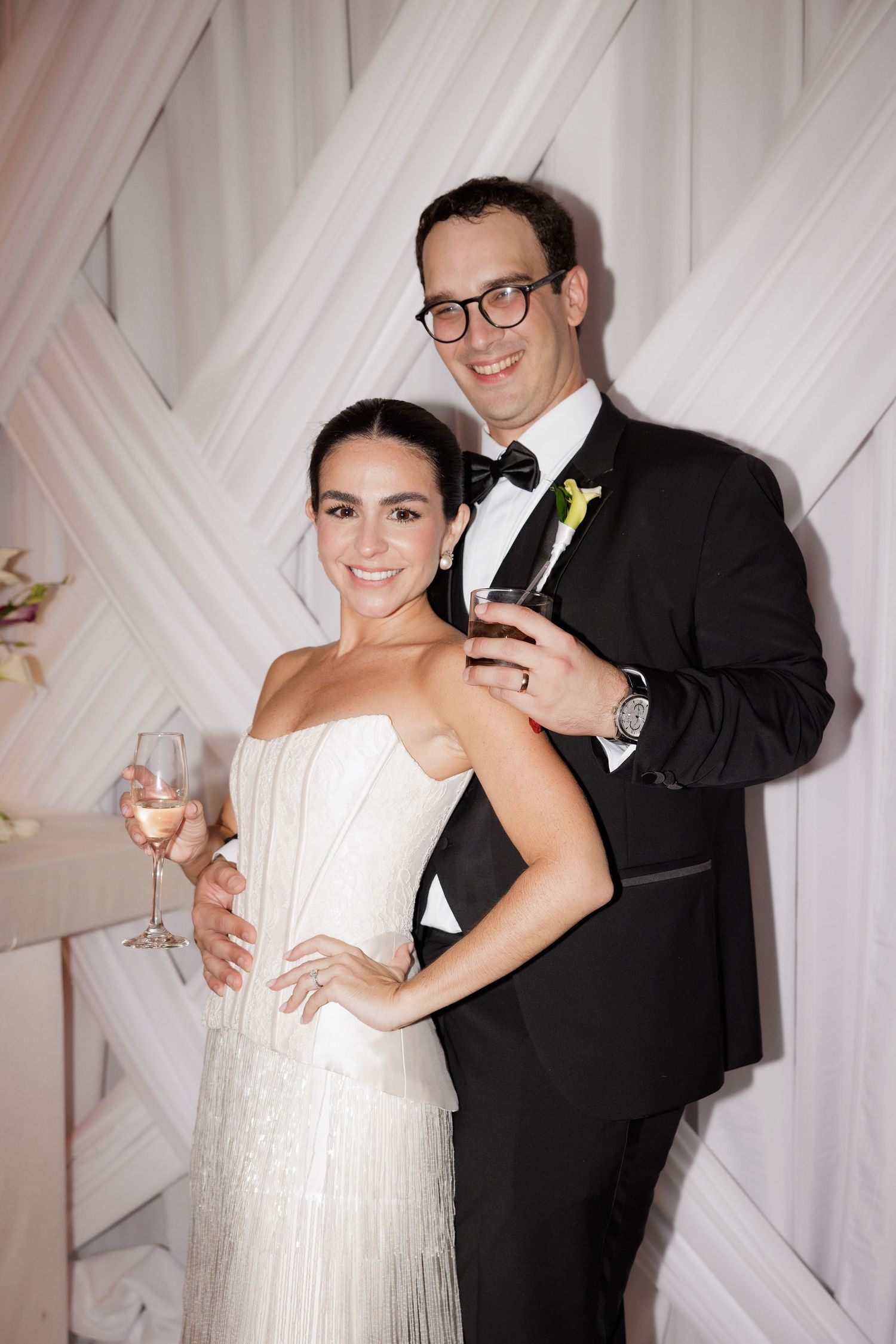 A wedding couple shares playful moments in front of a white geometric backdrop during their reception celebration.