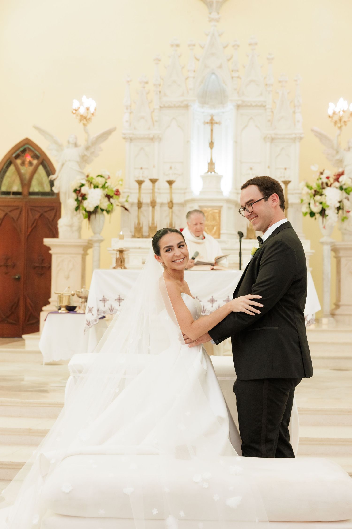 Wedding couple stands at ornate white altar during their church ceremony.