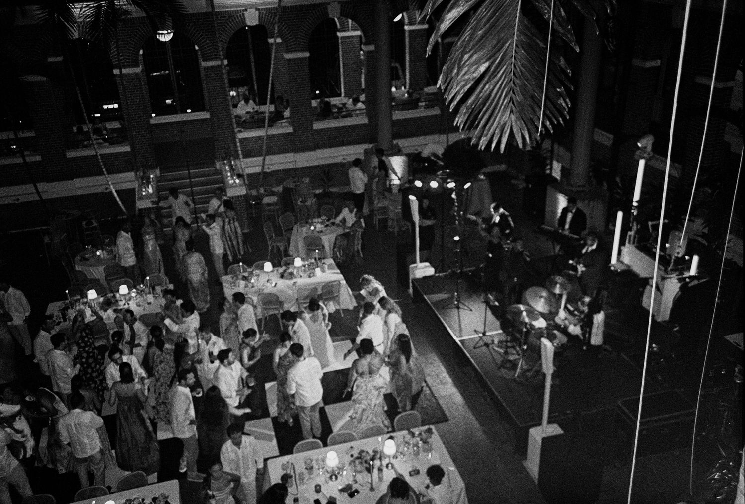 Aerial black and white view of a wedding reception with guests mingling around decorated tables indoors.