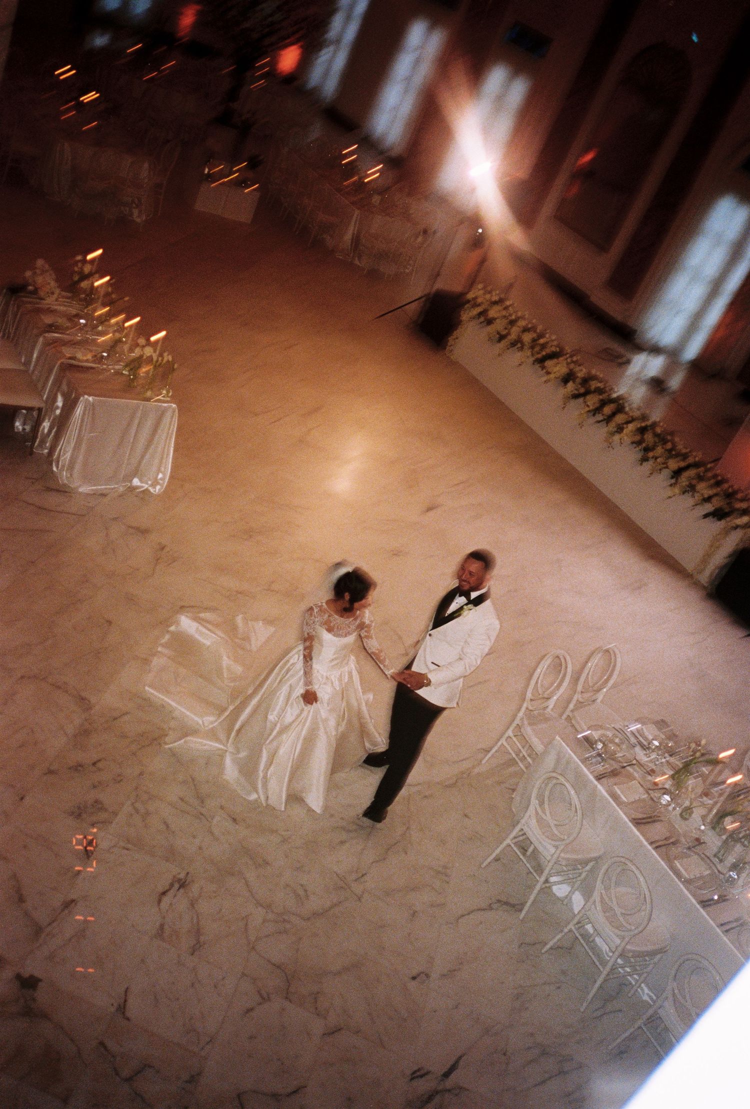 Aerial view of bride and groom sharing first dance on marble floor in elegant wedding reception.