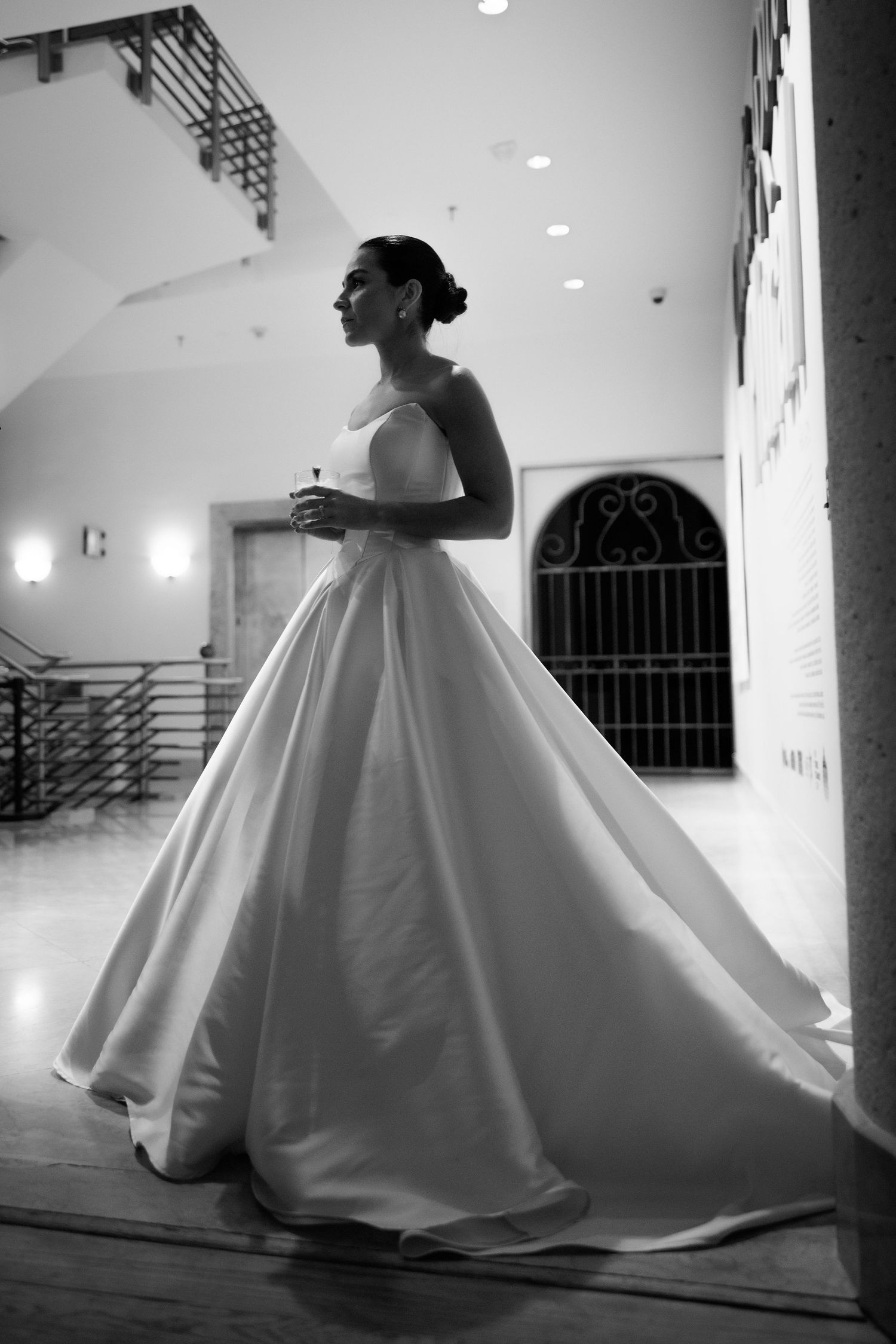 A bride in a voluminous white ballgown twirls gracefully in a modern architectural space.