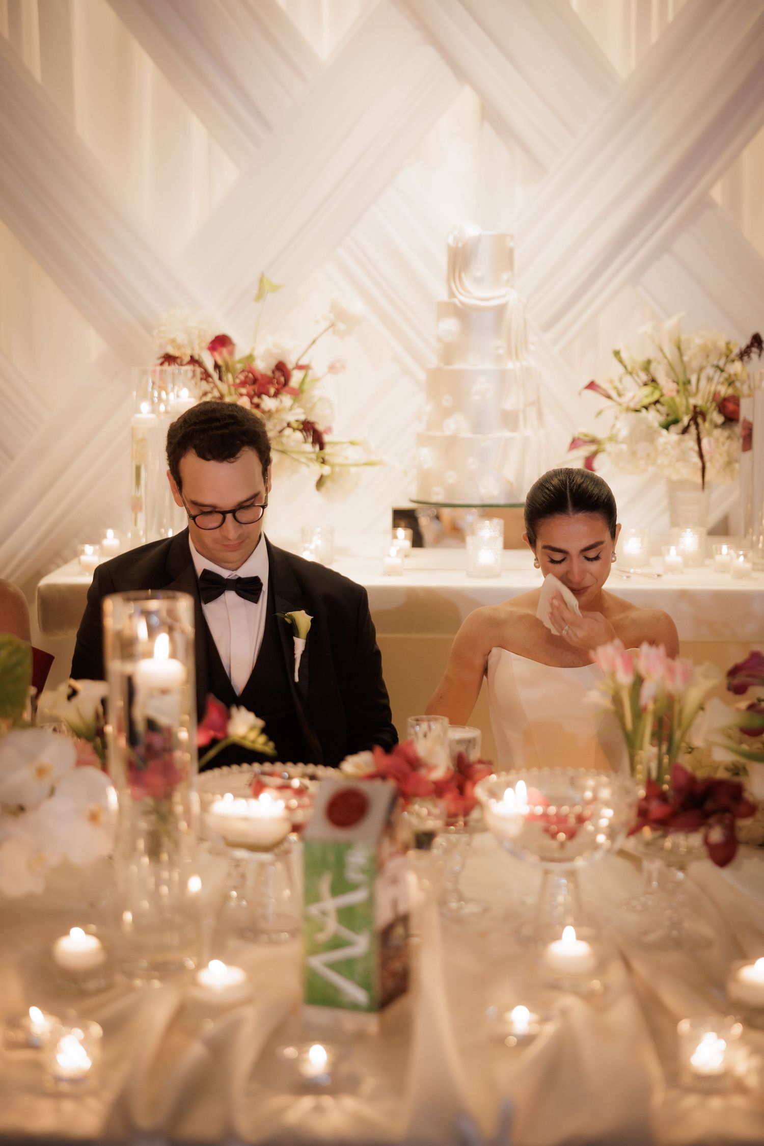Elegant wedding reception table setting with white draping, candles, and floral centerpieces creating a romantic atmosphere.
