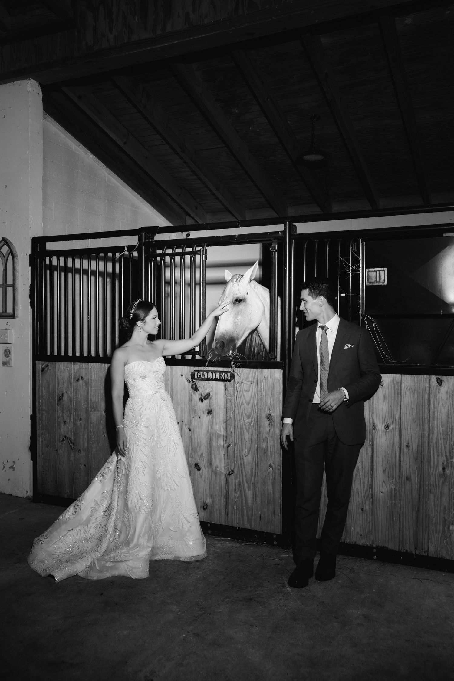Black and white photo of wedding couple posing in rustic wooden horse stables.