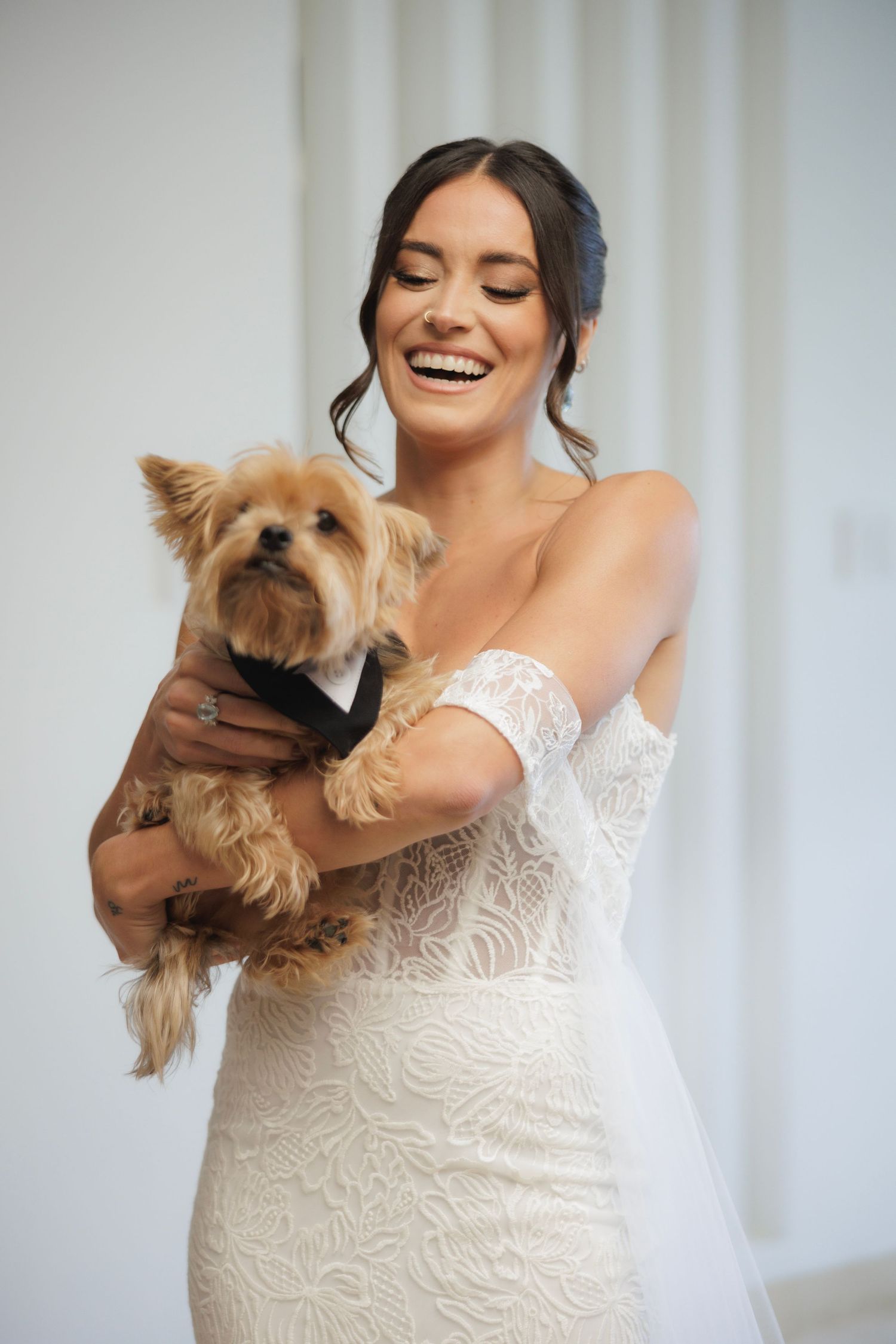 Joyful moments between a bride in a lace gown and a small Yorkshire terrier dog.