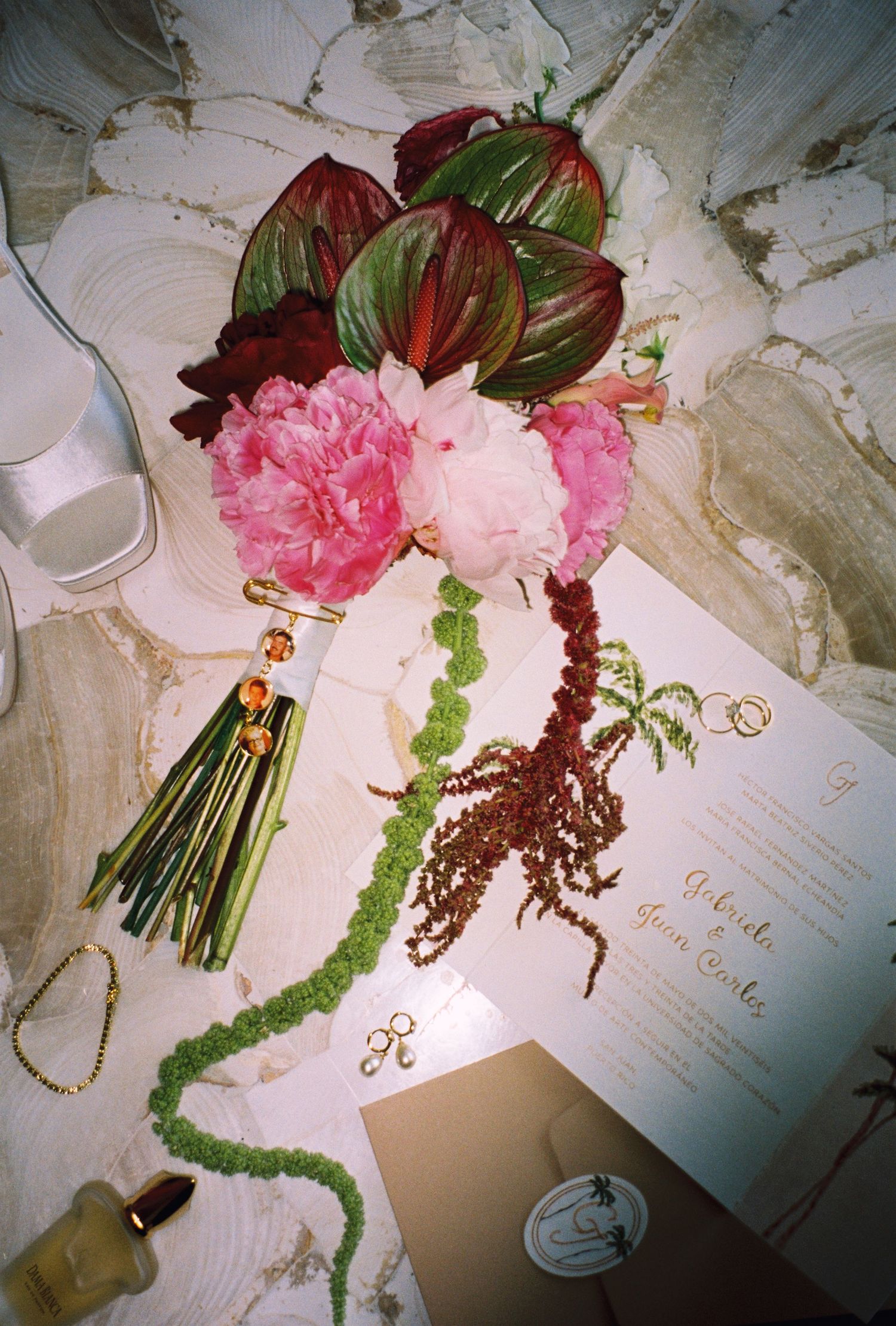 Elegant wedding flat lay with pink peonies, tropical leaves, gold jewelry, and calligraphy stationery on marble surface.