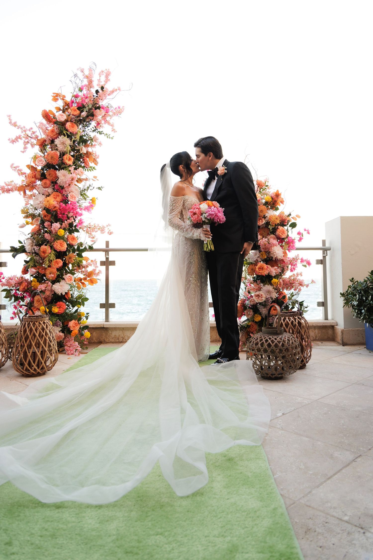 Elegant wedding ceremony setup with coral and pink floral arches on an oceanfront terrace.
