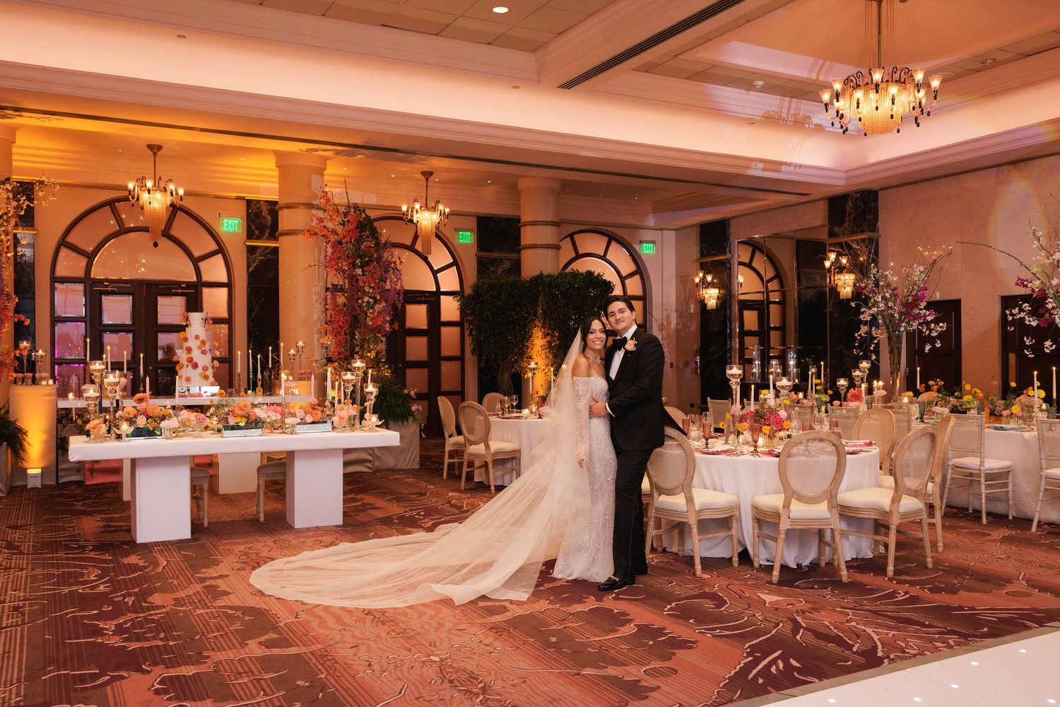 Luxurious hotel ballroom set up for a wedding reception with round tables and ornate chandelier lighting.