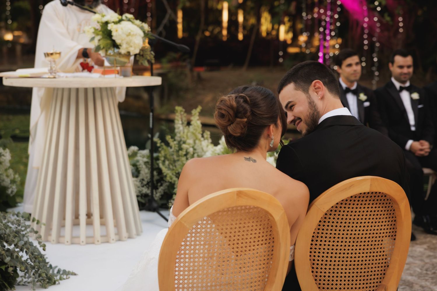 Intimate outdoor wedding moment with rattan chairs and elegant decor at dusk.