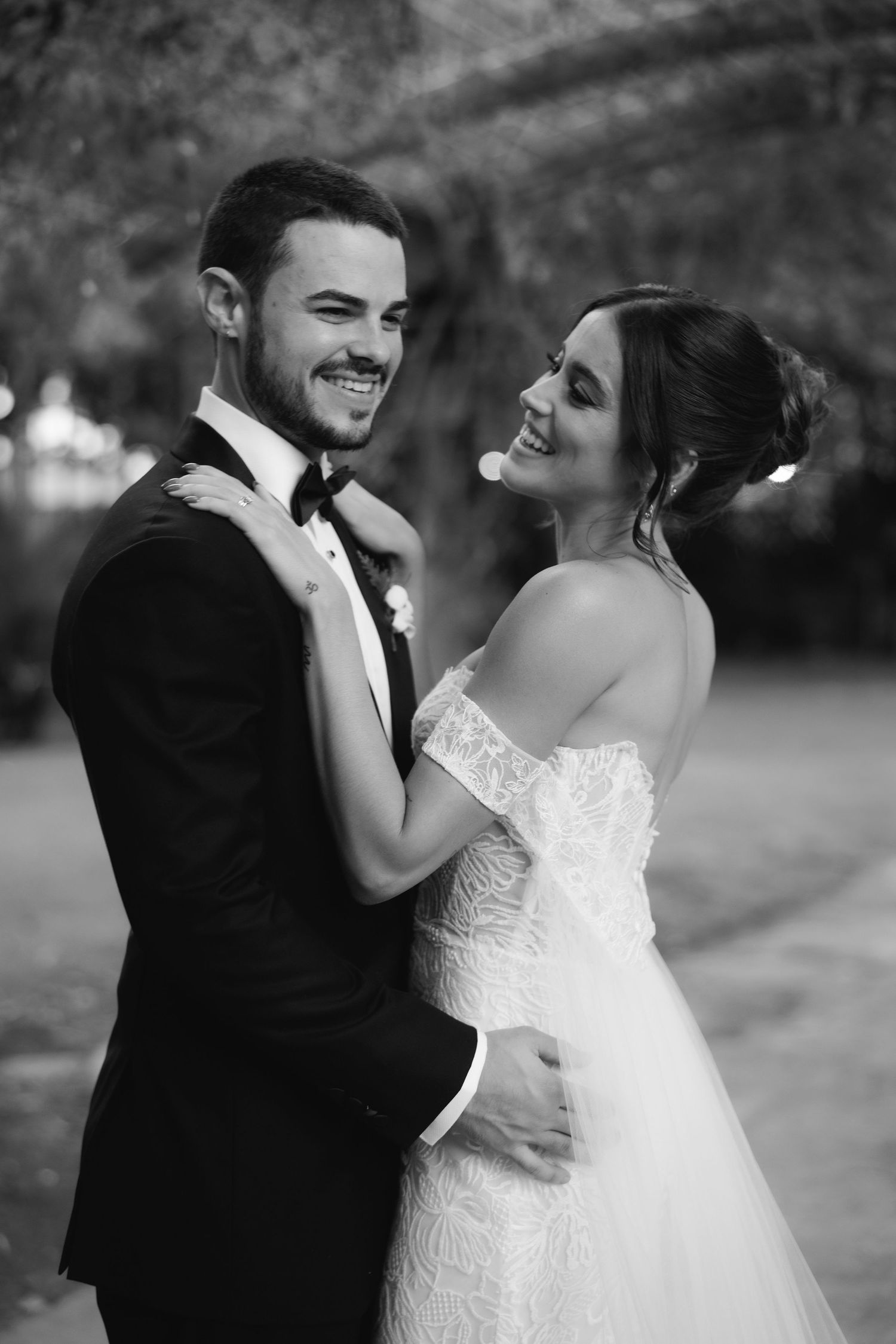 A black and white wedding portrait capturing a joyful candid moment between newlyweds.
