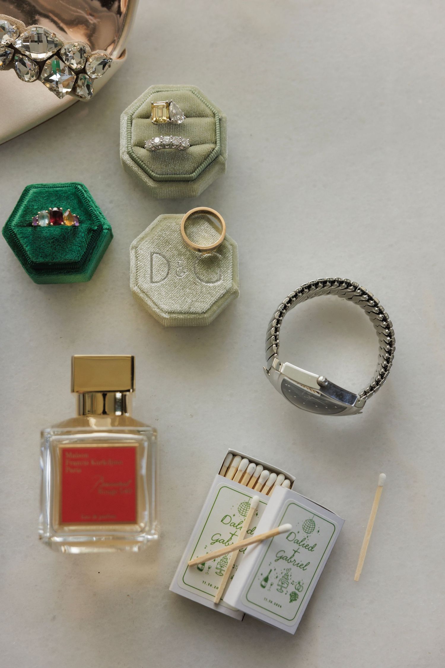 Wedding accessories including rings, ring boxes, perfume and jewelry arranged on a light surface.