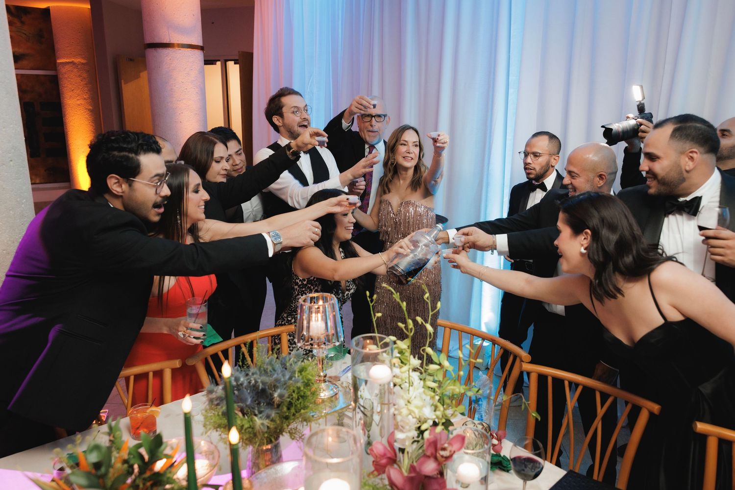 Wedding reception guests at a banquet table raise their glasses in a festive toast during dinner celebration.