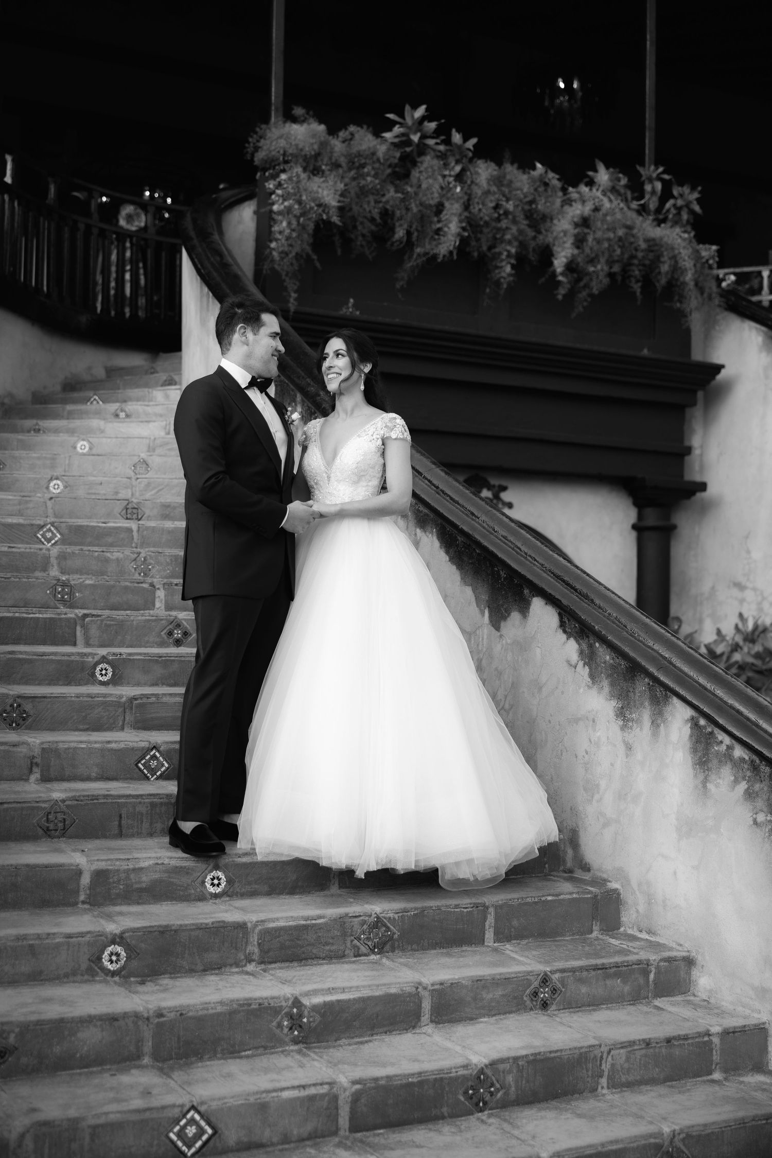 A dramatic black and white image of newlyweds ascending vintage stone stairs with decorative tile details.