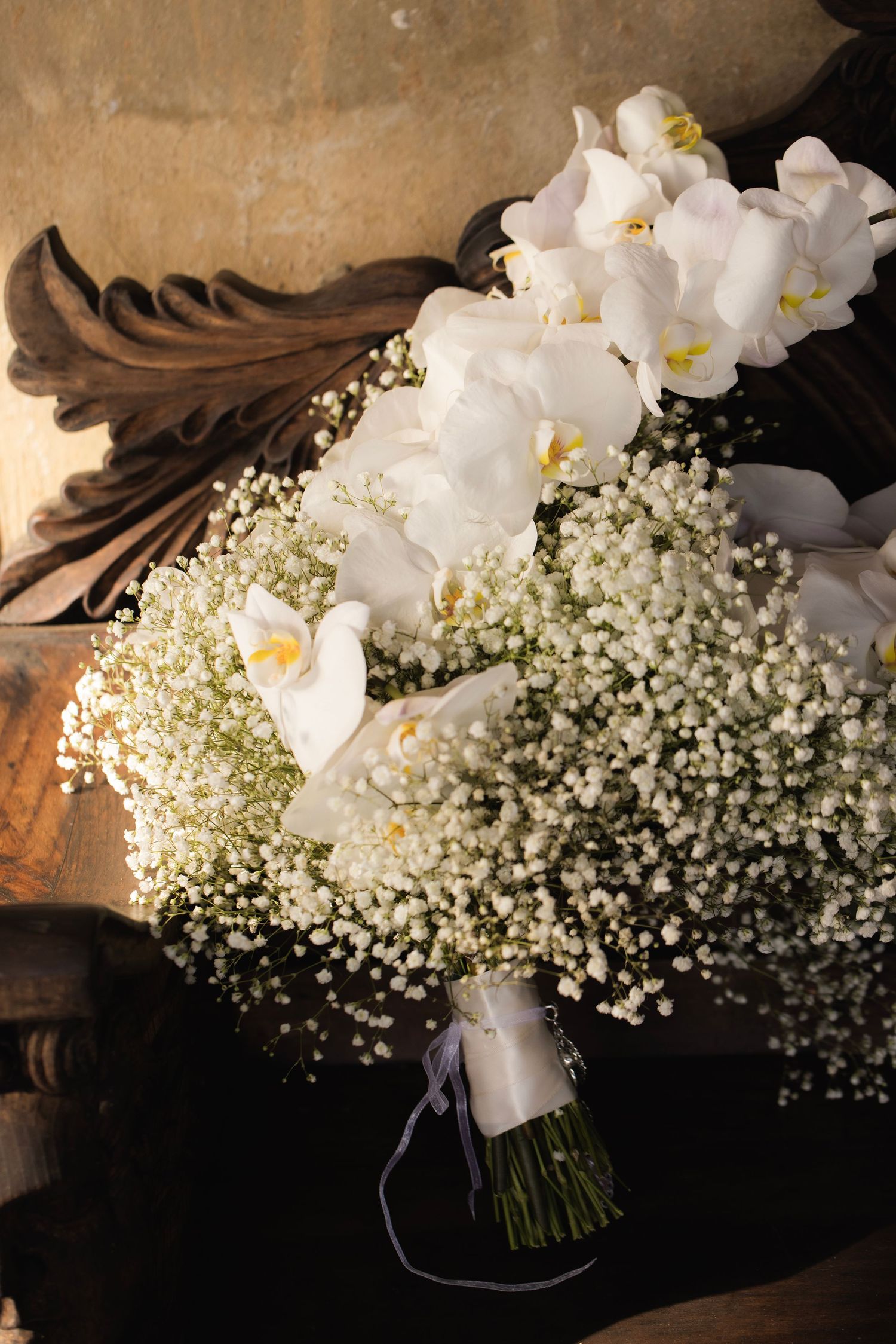 Elegant white orchids and delicate baby's breath flowers arranged in a cascading bridal bouquet.