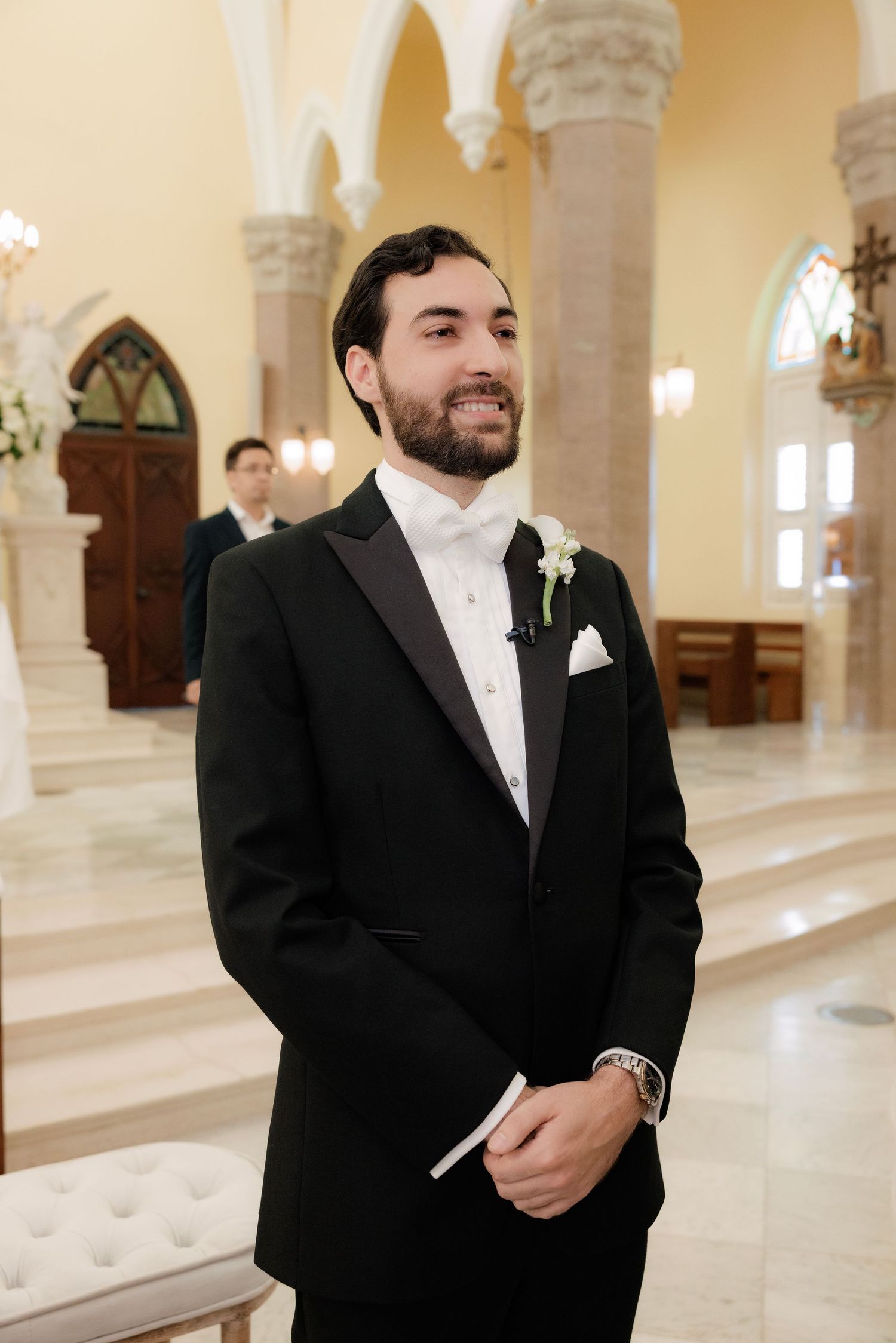 A groom stands in an ornate church interior with arched columns and warm lighting.