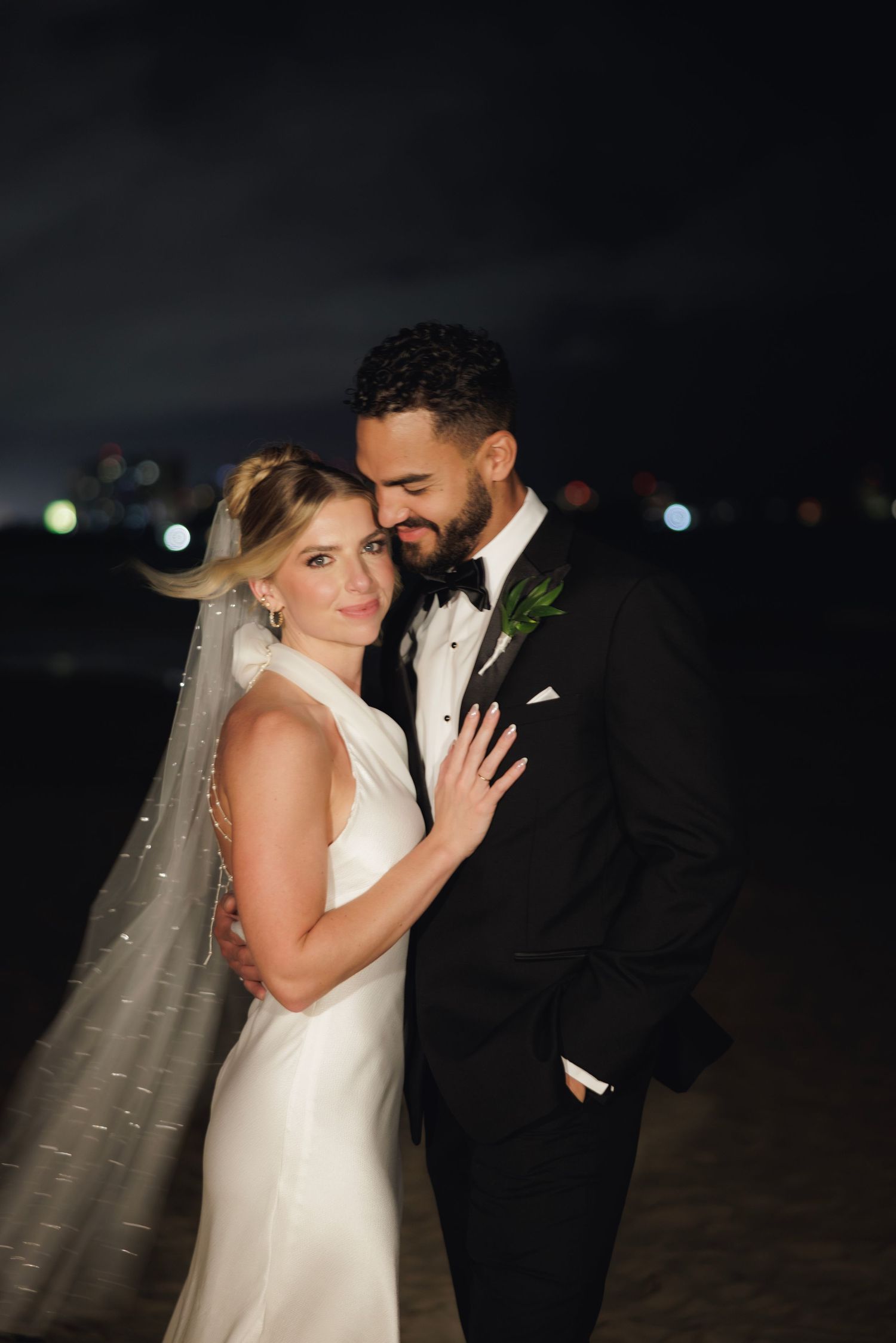 A romantic nighttime wedding portrait shows a couple embracing, with the bride in white and groom in black tuxedo.