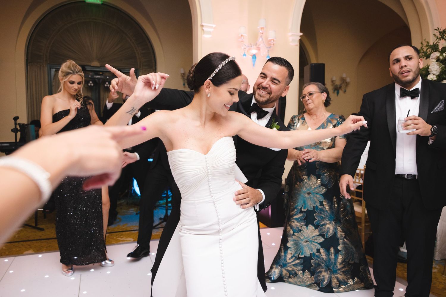 Wedding celebration on dance floor with bride in white dress dancing surrounded by party guests in formal attire.