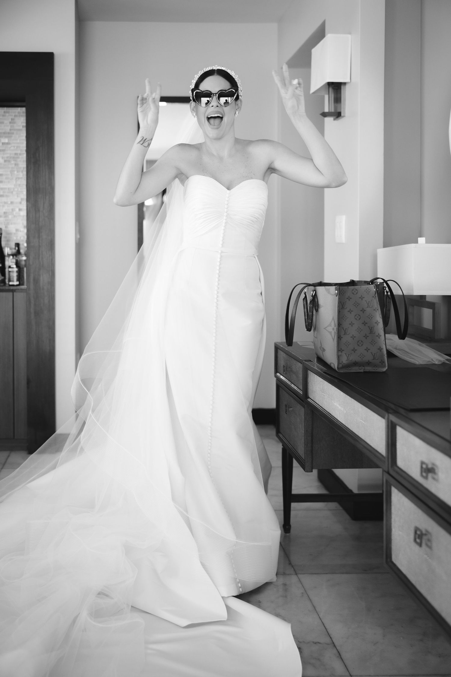 A joyful bride in glasses and a strapless white wedding gown poses expressively in black and white.