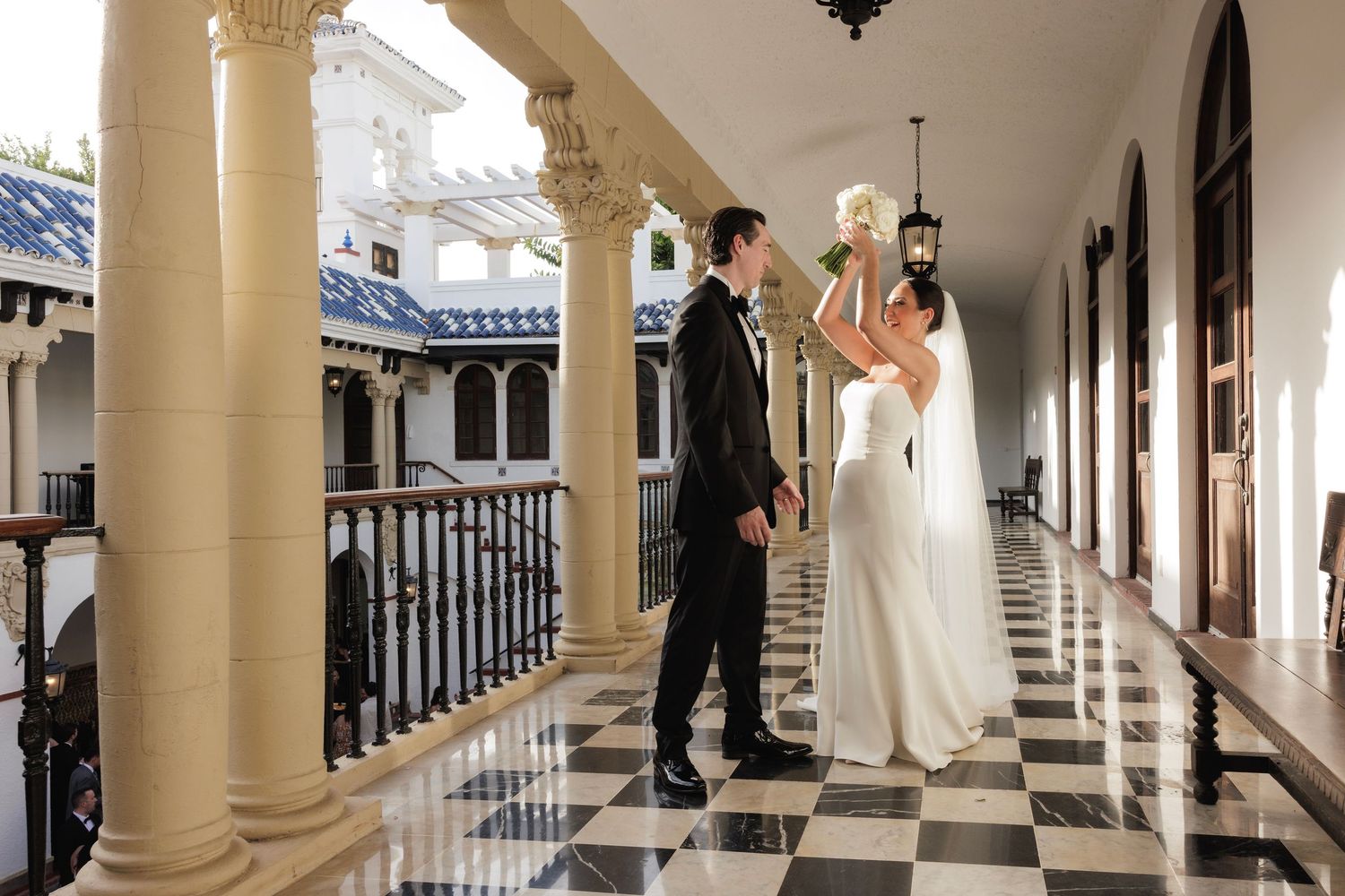 A bride and groom walk along an elegant colonnade hallway with beautiful architectural pillars at their wedding.