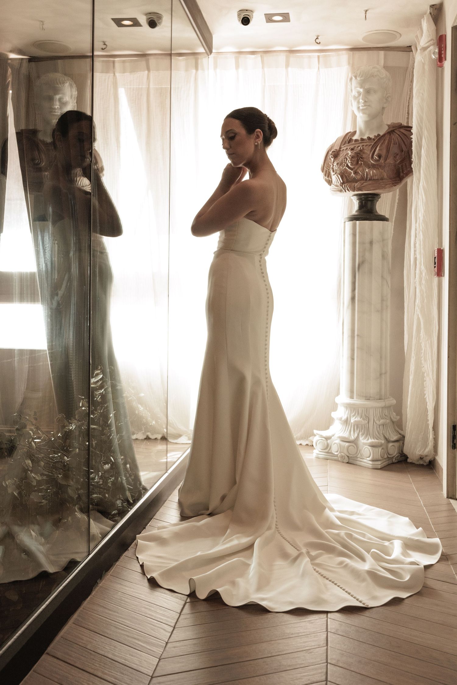 Elegant white wedding dress photographed in a light-filled room with mirrors creating reflective angles.