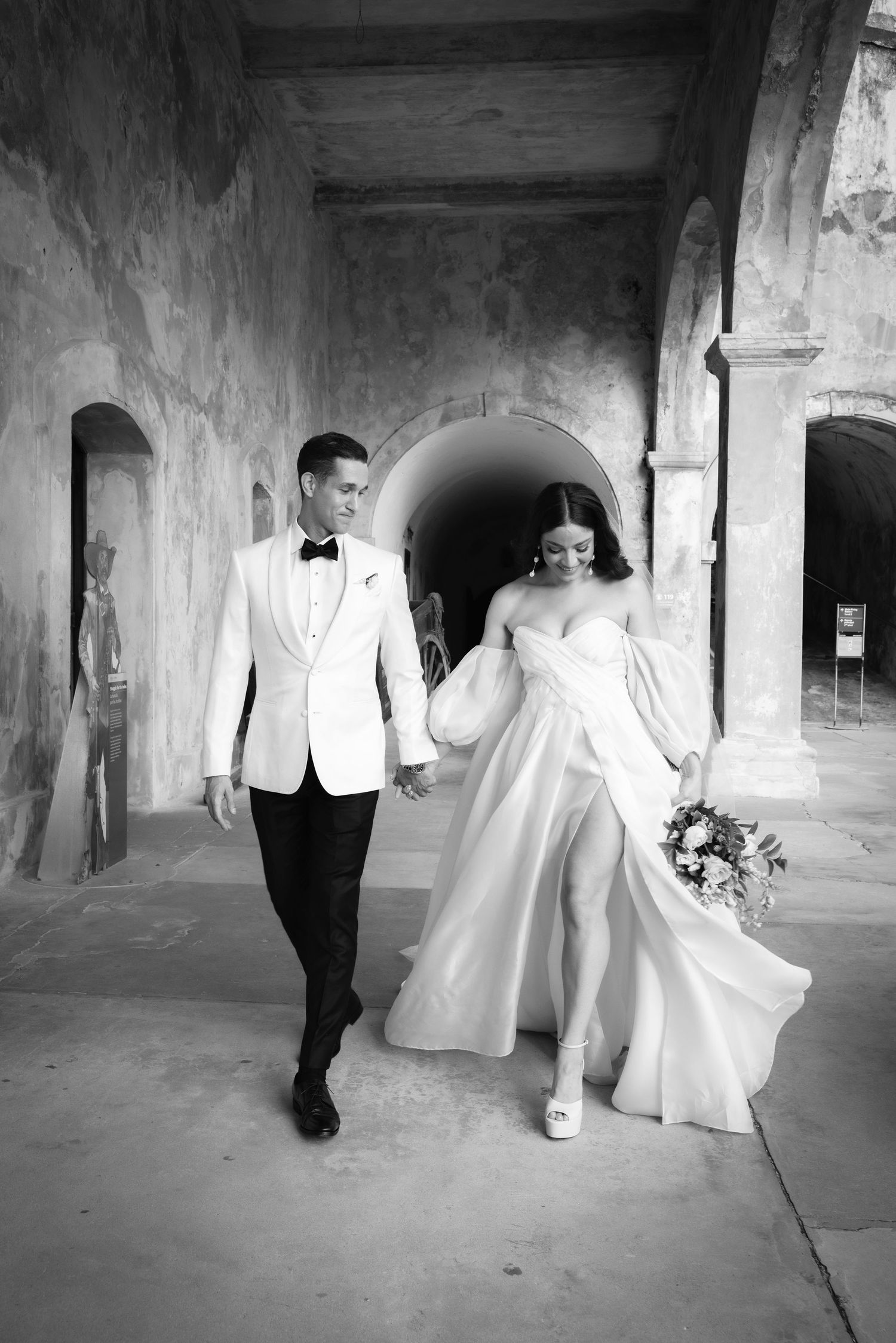 Black and white wedding portraits captured in a historic stone colonnade with dramatic shadows.