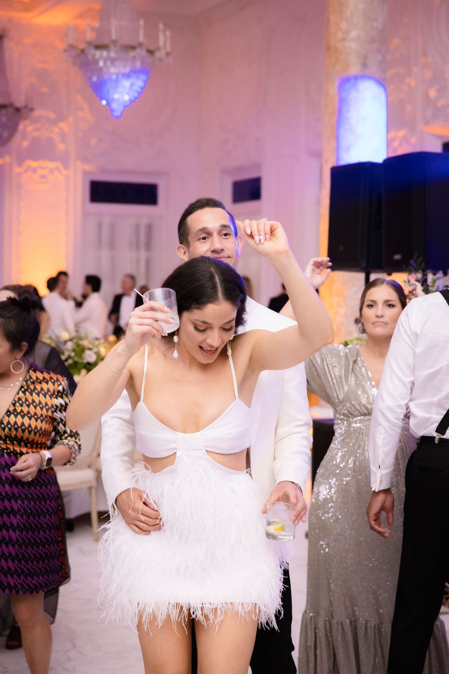 Wedding reception dance floor scene with guests in formal attire dancing energetically in an elegantly lit venue.