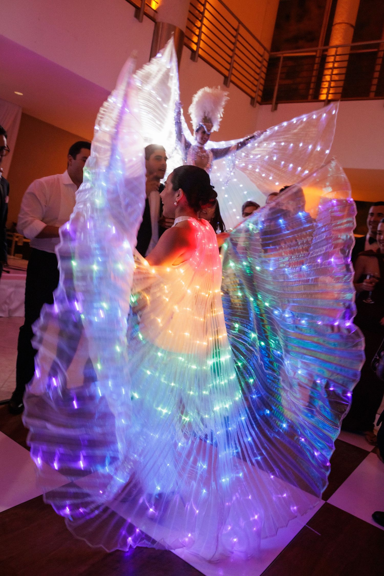 A dancer performs with illuminated LED wings creating a stunning light display at a wedding reception.