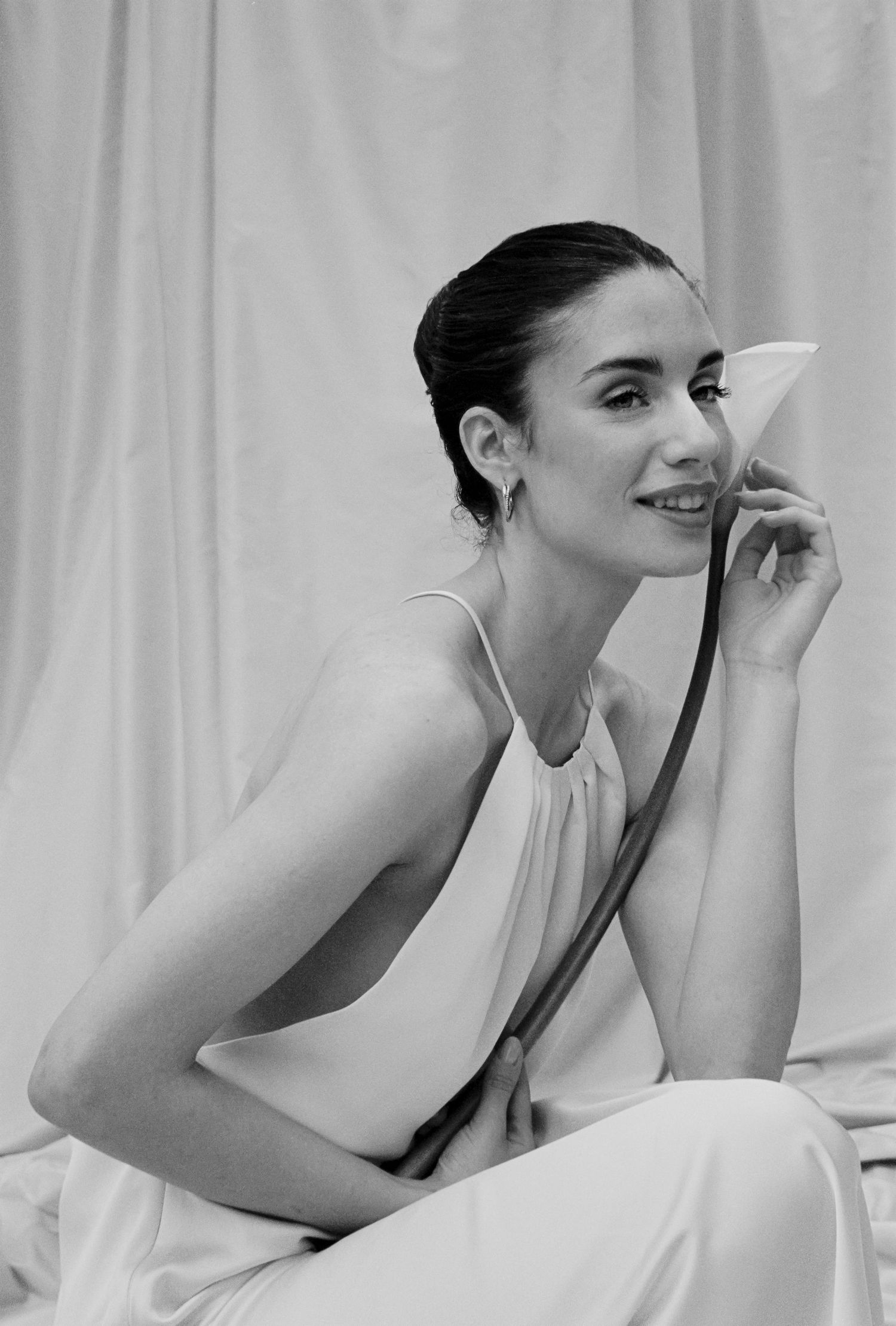 Elegant woman in a white halter dress poses with a flower in a soft black and white portrait.