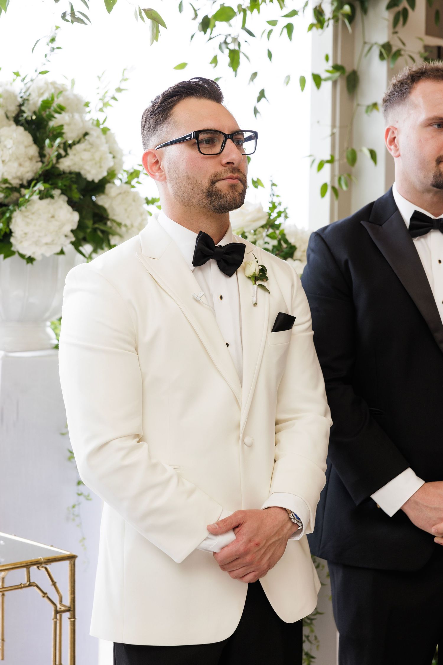 Groomsmen in white and black tuxedos standing in line at wedding ceremony.
