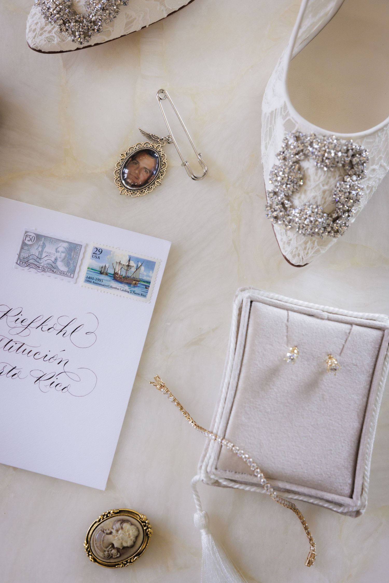 Wedding accessories including embellished shoes, jewelry, and vintage cameos arranged with invitation stationery.