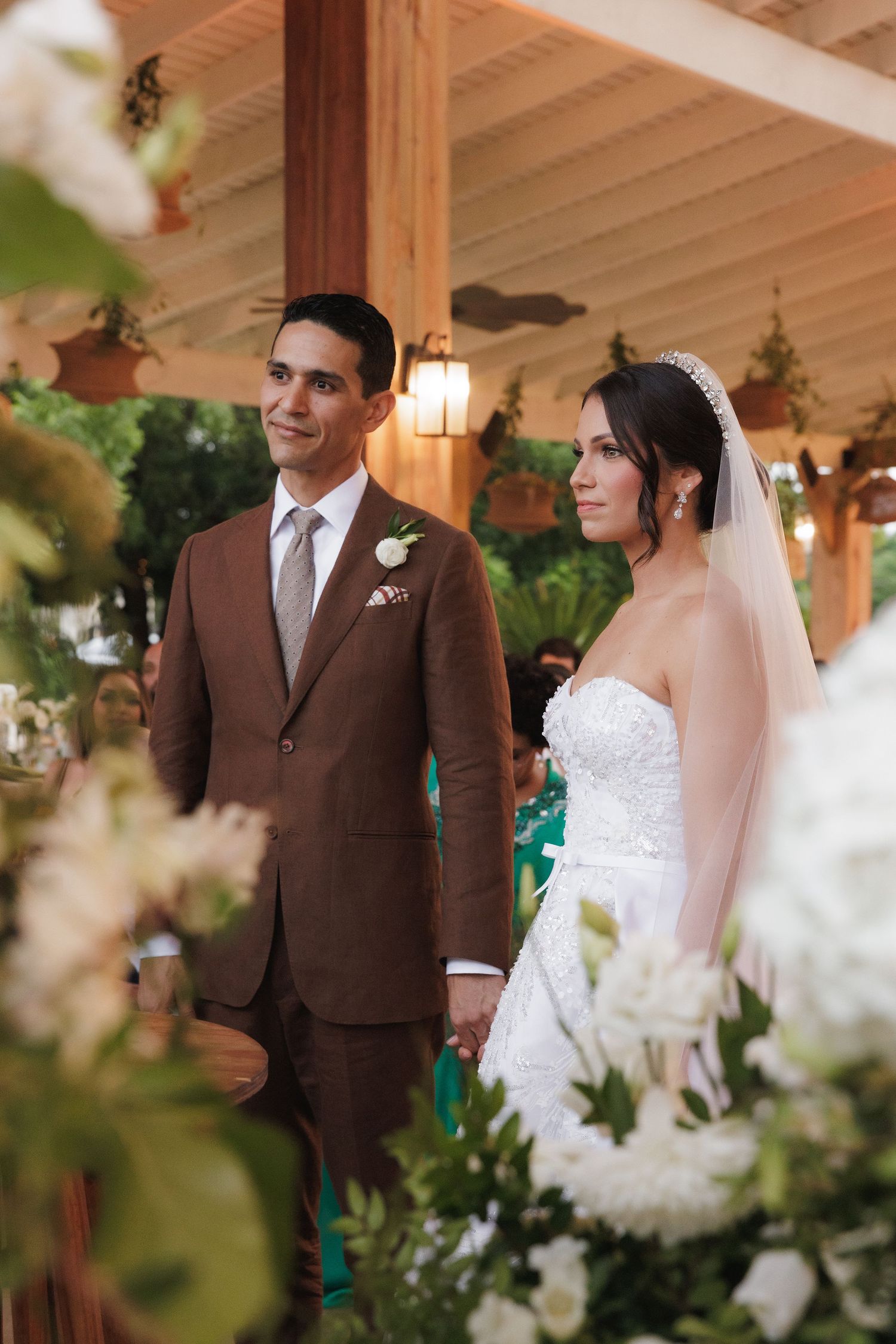Elegant wedding ceremony under wooden beams with white floral decorations and soft lighting.