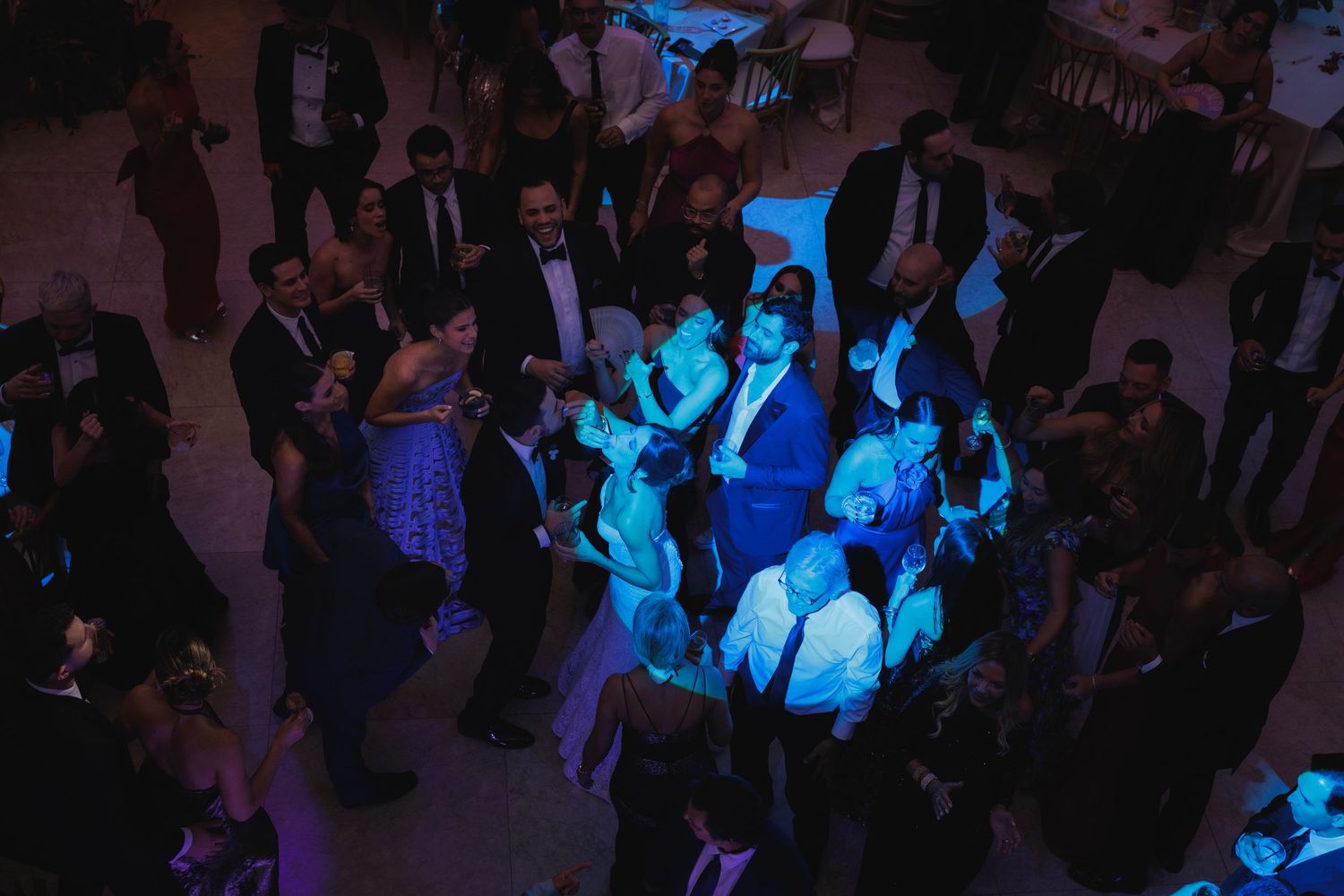 Wedding reception dance floor filled with guests under blue ambient lighting.