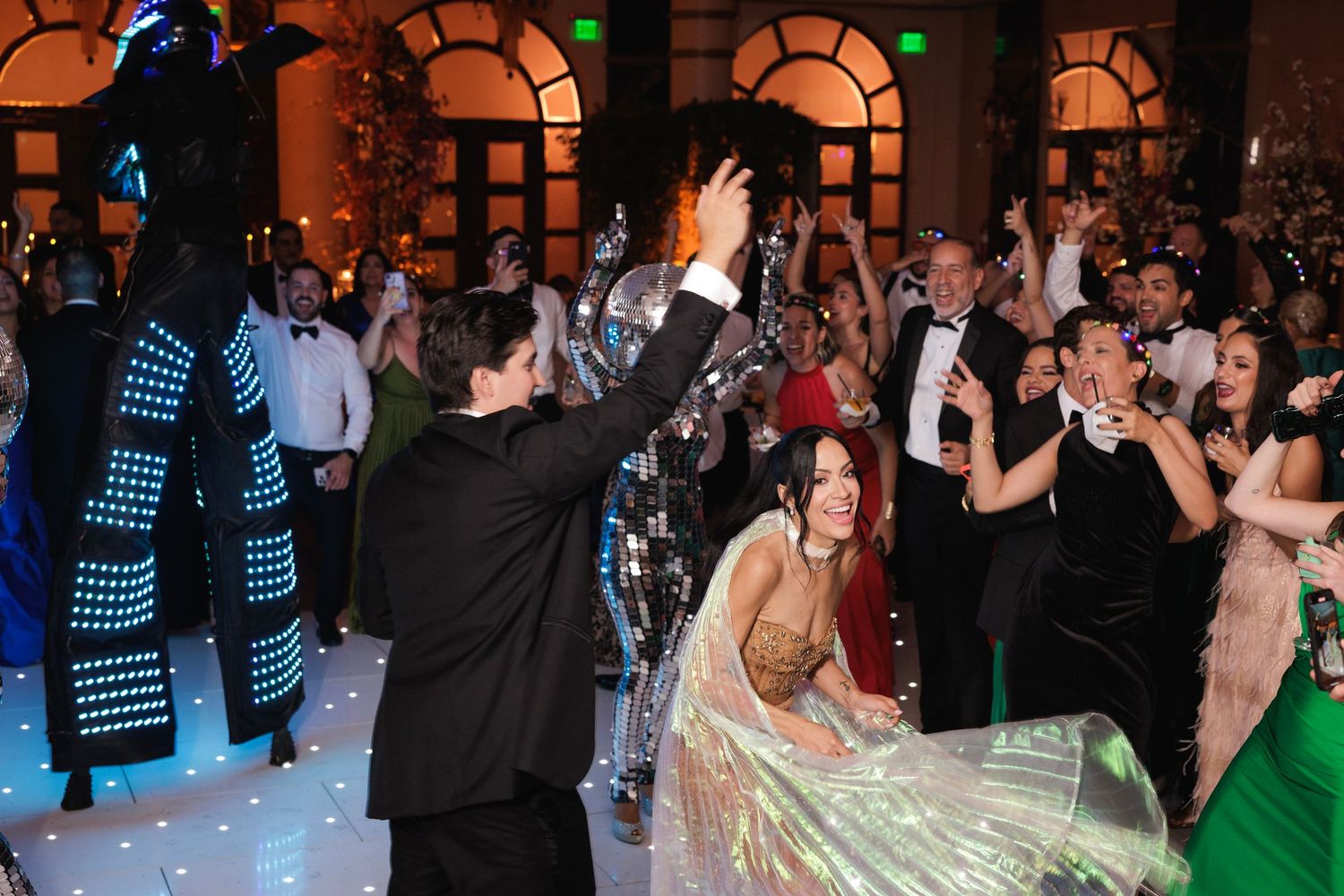 Large crowd of people dancing and celebrating on an illuminated dance floor at a nightclub or party event.