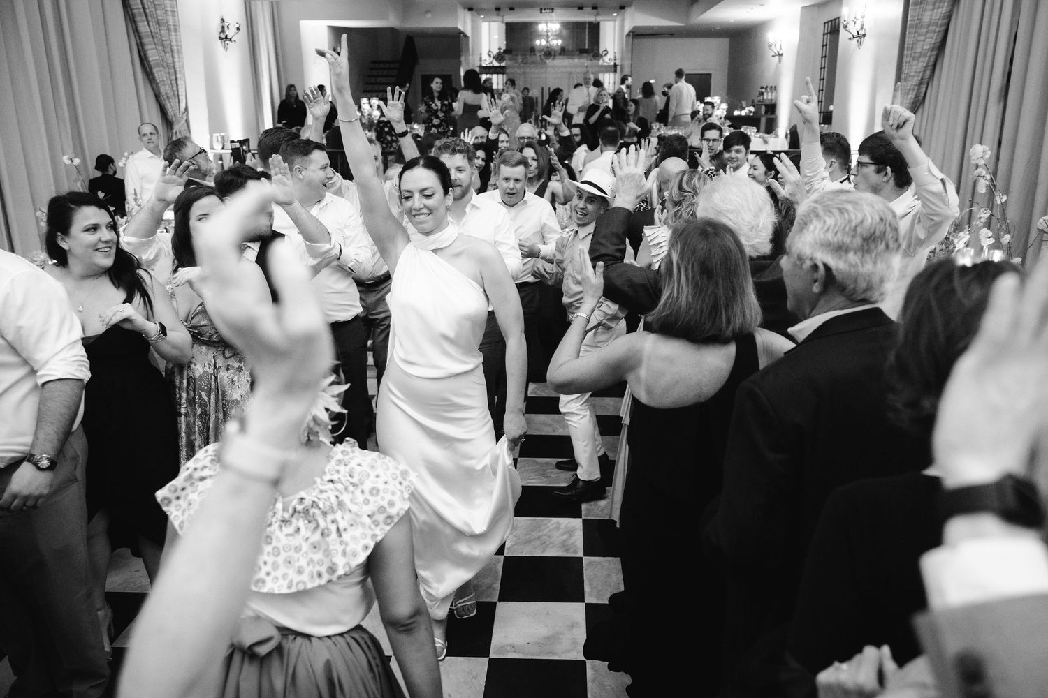 A festive crowd of people dancing and celebrating at a lively black and white wedding reception.